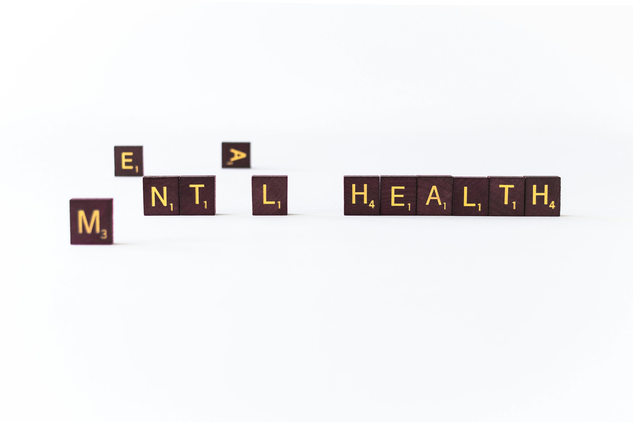 Scrabble tiles spell out 'MENTAL HEALTH' on a white background.