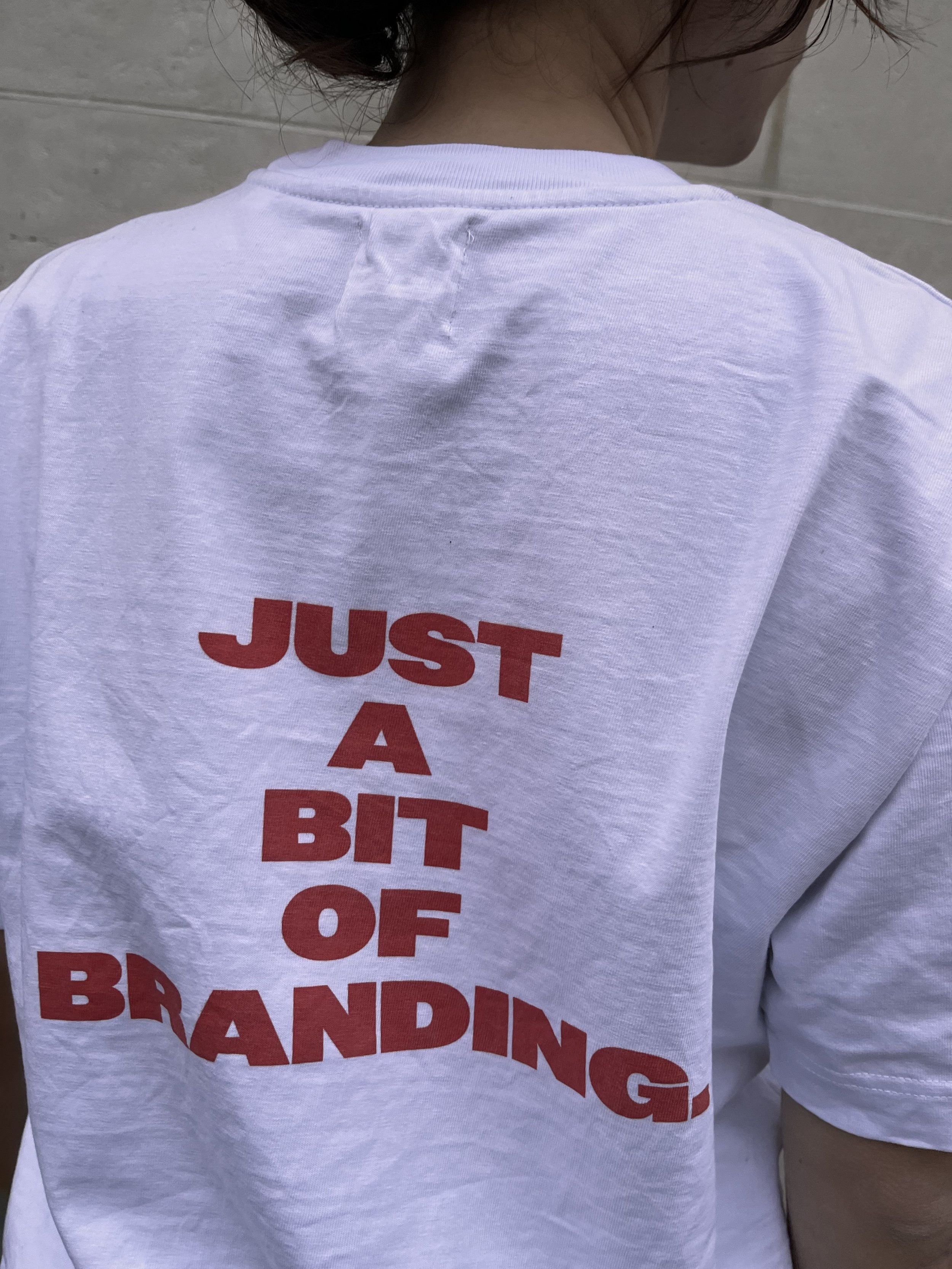 Photo zoomée d’un t-shirt blanc porté dans les rues parisiennes et arborant un visuel orange avec inscrit ‘Just A bit Of Branding’