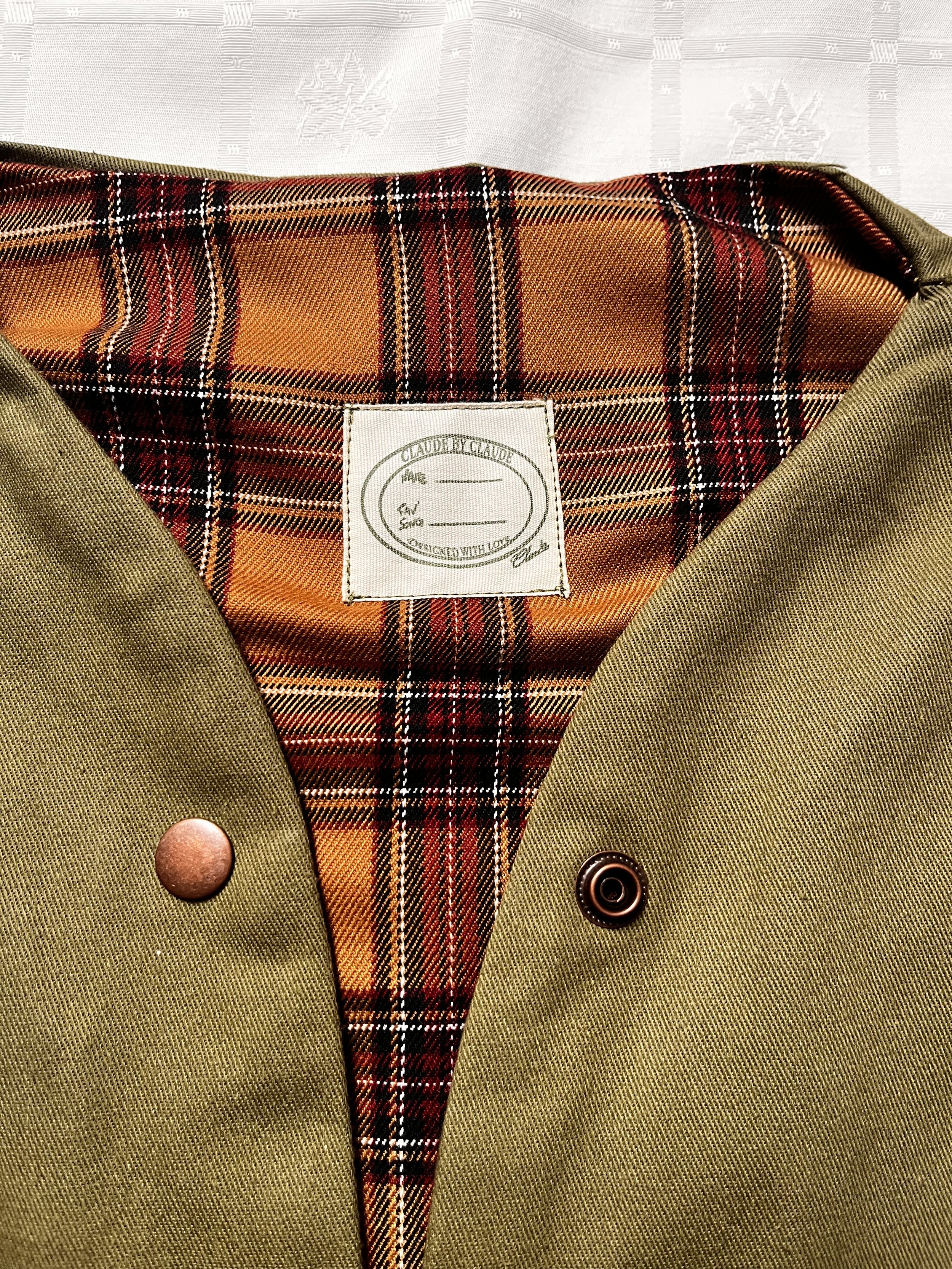 Zoom de l’étiquette d’un intérieur de vêtement confectionné dans une gabardine de coton vert foncé et une doublure en tartan à carreaux ocre