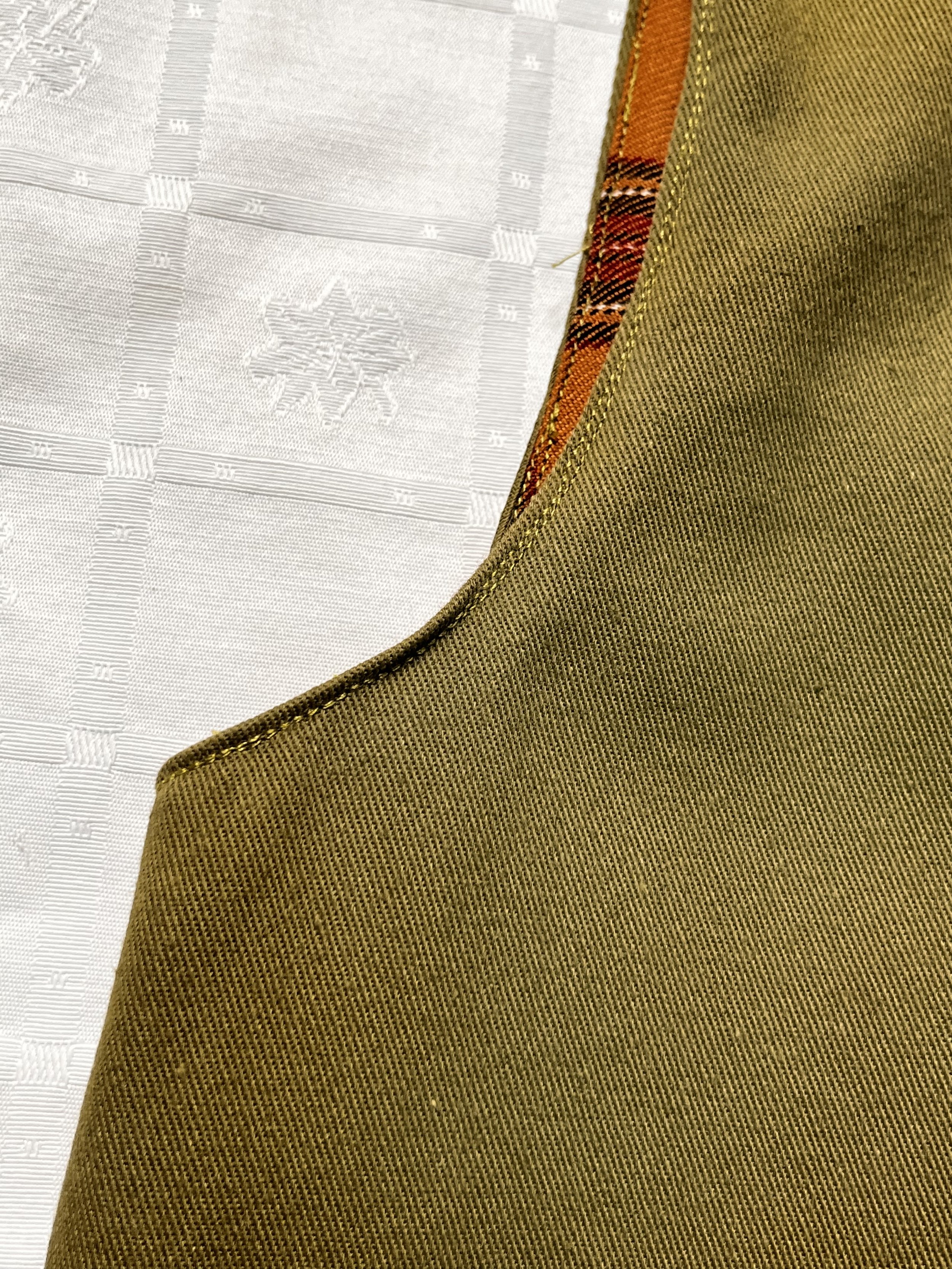 Détail de l’emmanchure d’un gilet confectionné dans une gabardine de coton vert foncé et une doublure en tartan à carreaux ocre