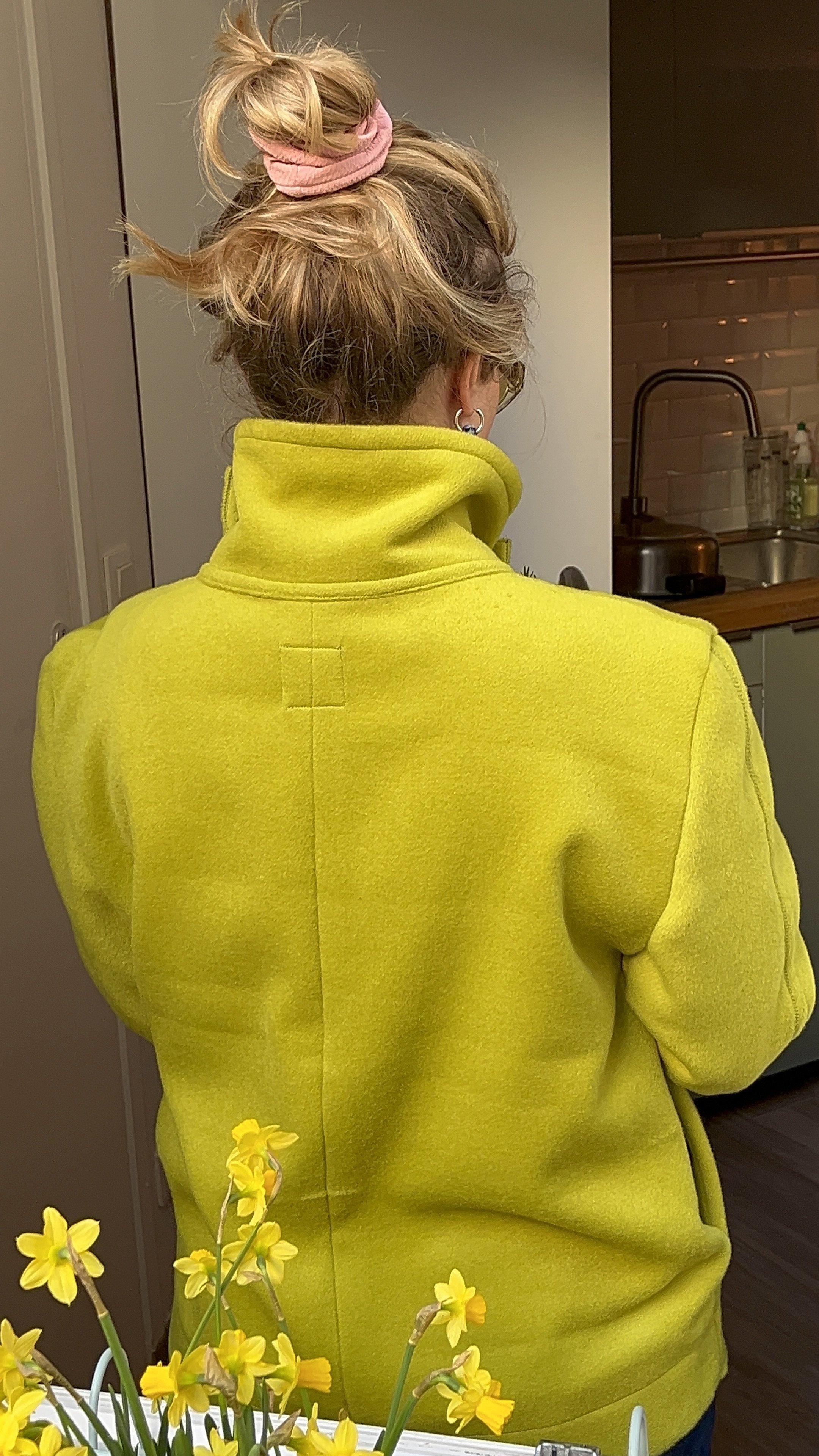 Photo d’une jeune femme blonde de dos, portant une veste en laine vert anis et cousue à la main