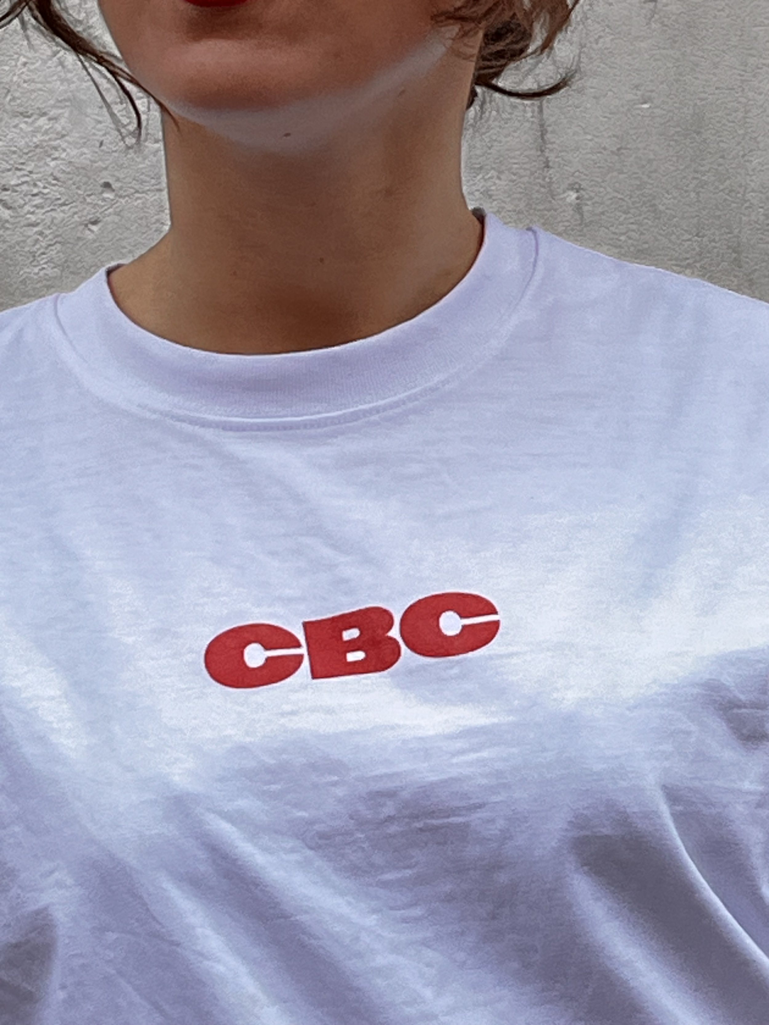 Zoom sur le buste d’un mannequin féminin posant dans les rues de paris et portant un t-shirt Claude by Claude Studios avec l’inscription ‘CBC’