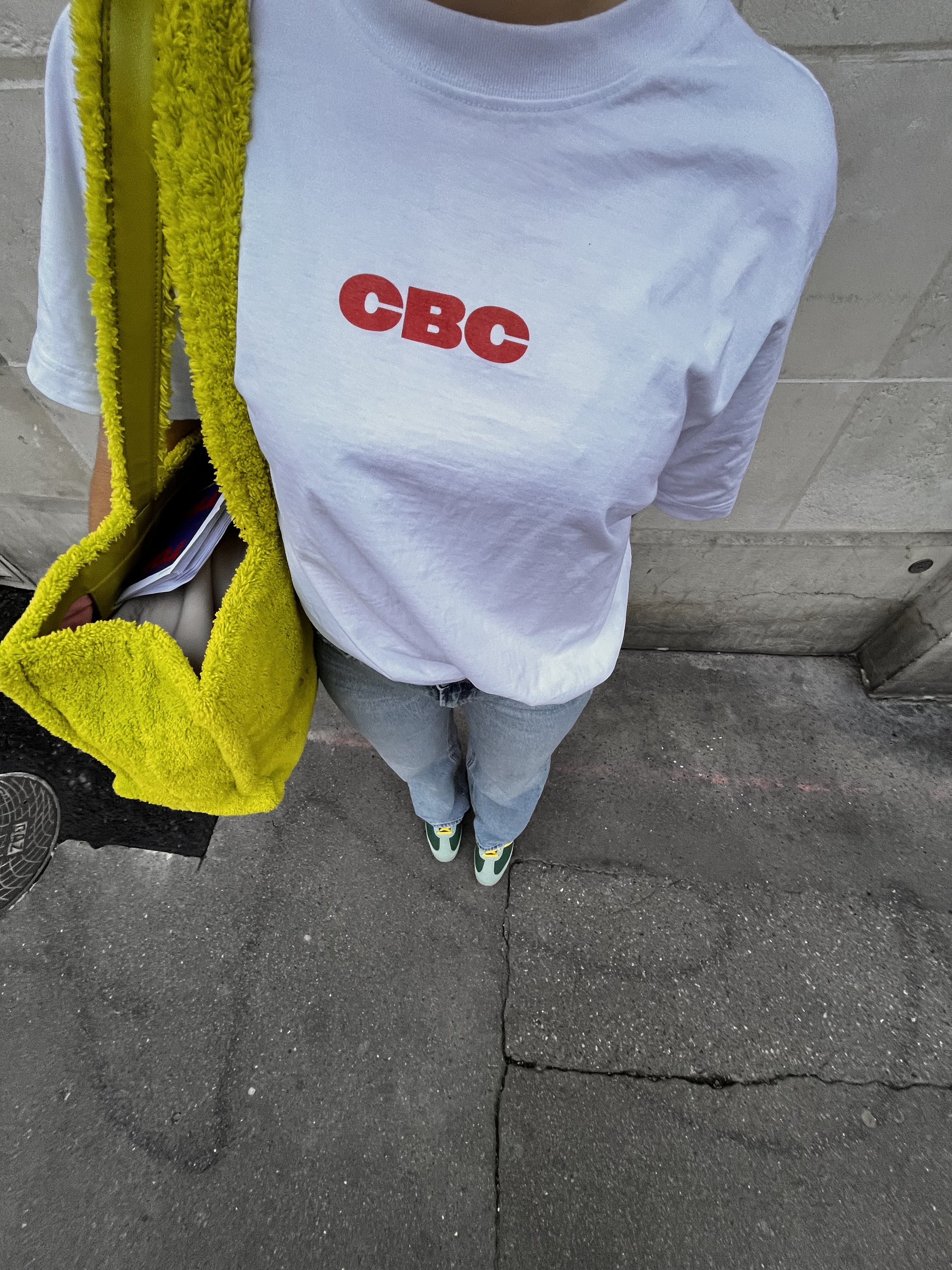 Photo prise de haut d’un mannequin féminin portant un t-shirt blanc avec écrit en orange soutenu, ‘CBC’ sur le devant