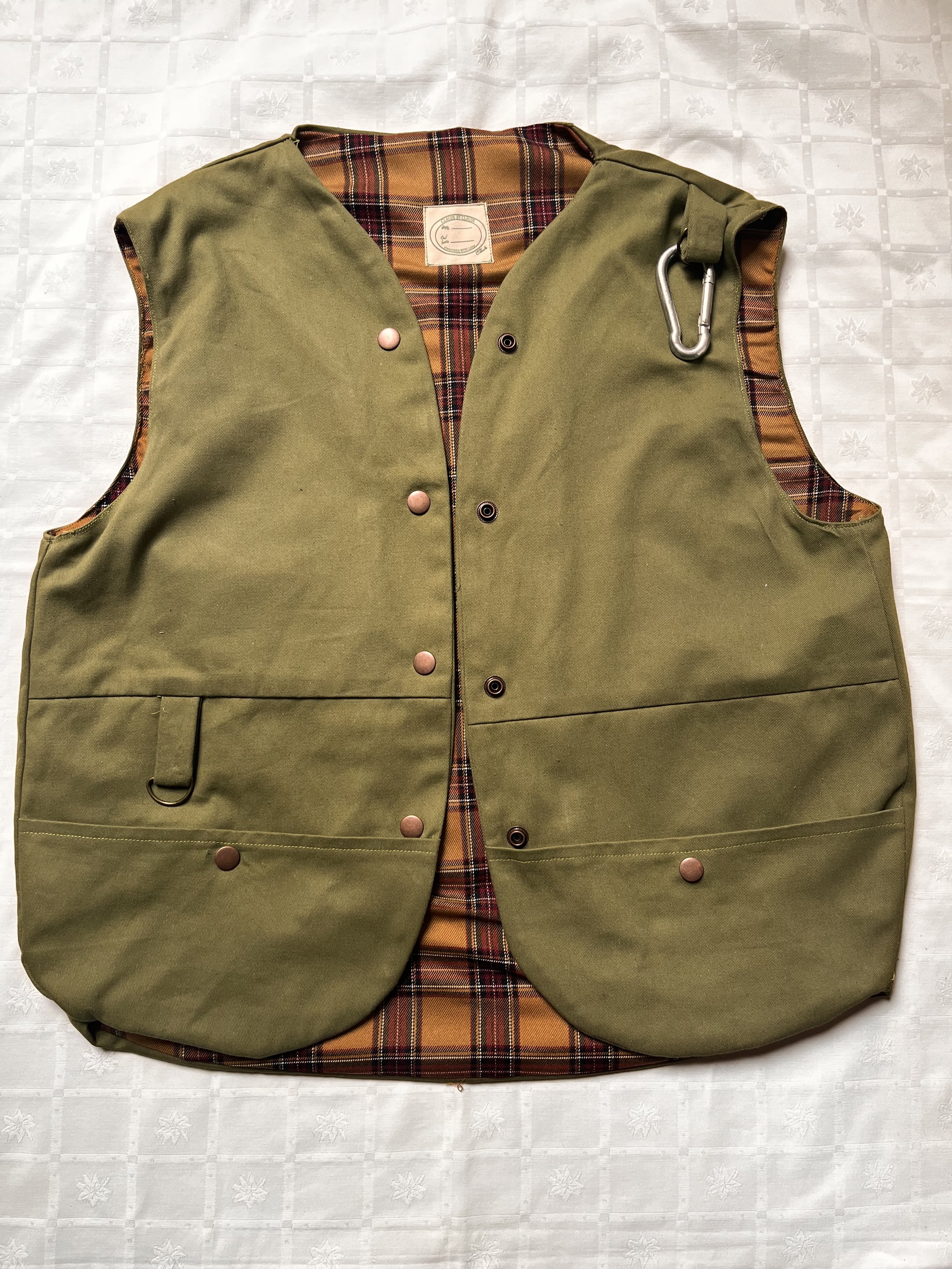 Gilet sans manche à boutons pressions, dans une gabardine de coton vert foncé et doublure tartan ocre