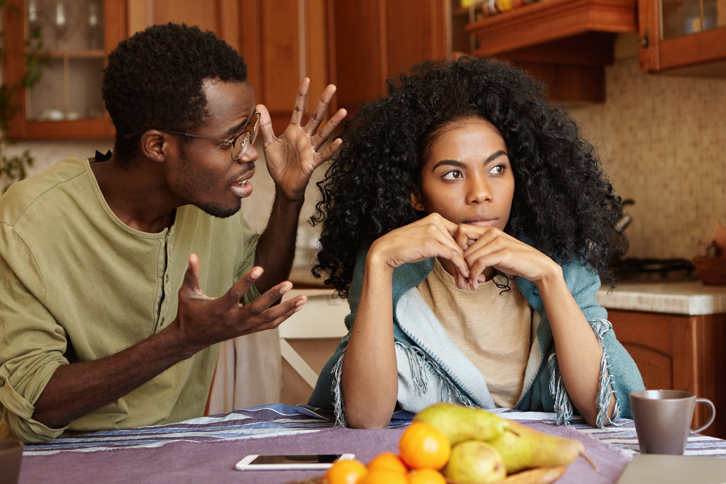 A couple in their kitchen where one partner is speaking with frustration while the other looks away showing the withdrawal that develops when criticism becomes a pattern in the relationship
