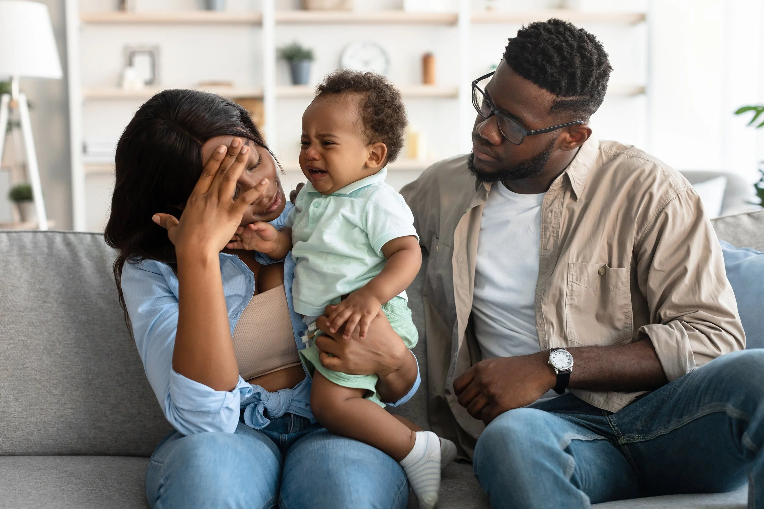 Black couple sitting together with baby, mother overwhelmed, postpartum relationship stress