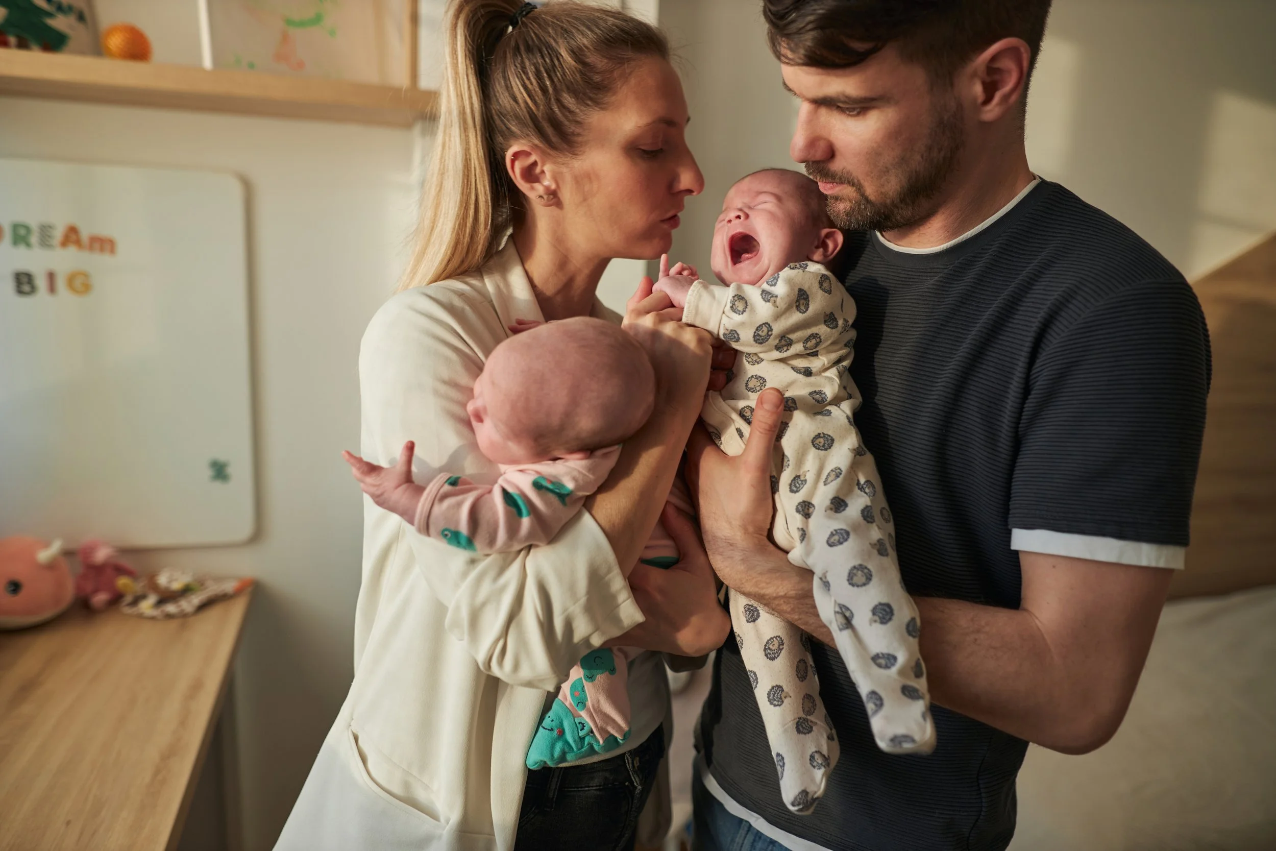 Postpartum couple holding new born twins that look overwhelmed.