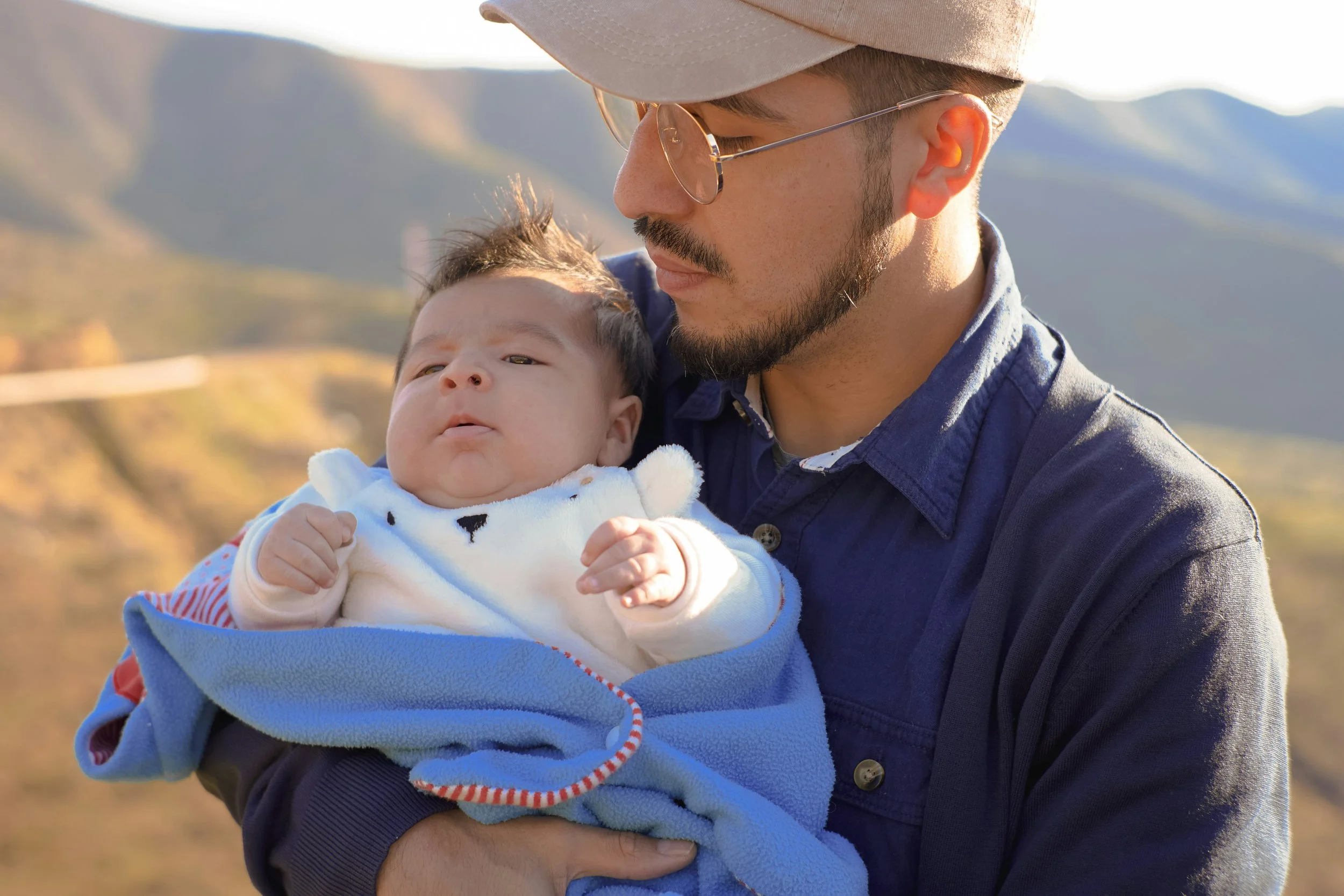 A father holding his baby while looking into the distance showing the emotional weight new fathers carry during the postpartum period.