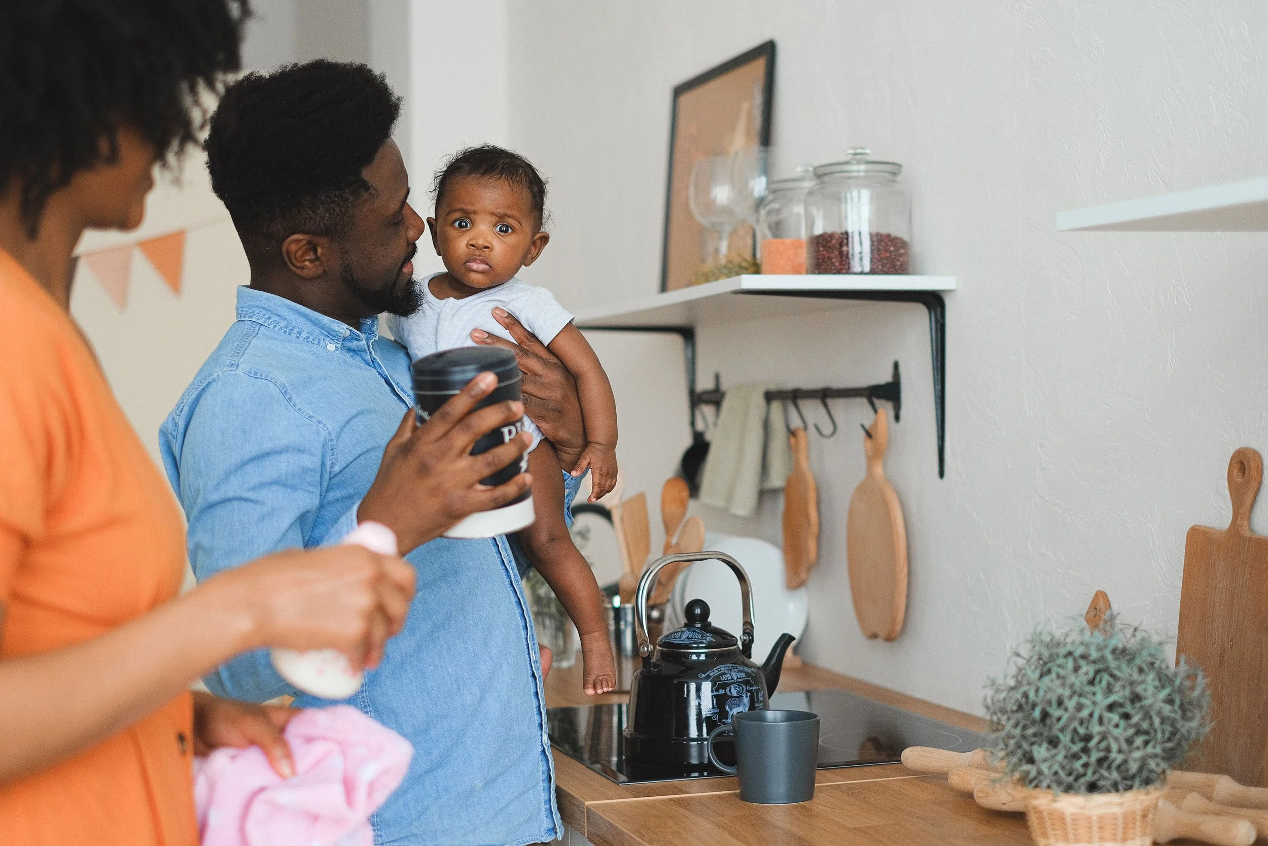Parents caring for their baby together in the kitchen, sharing the load instead of one partner carrying it alone