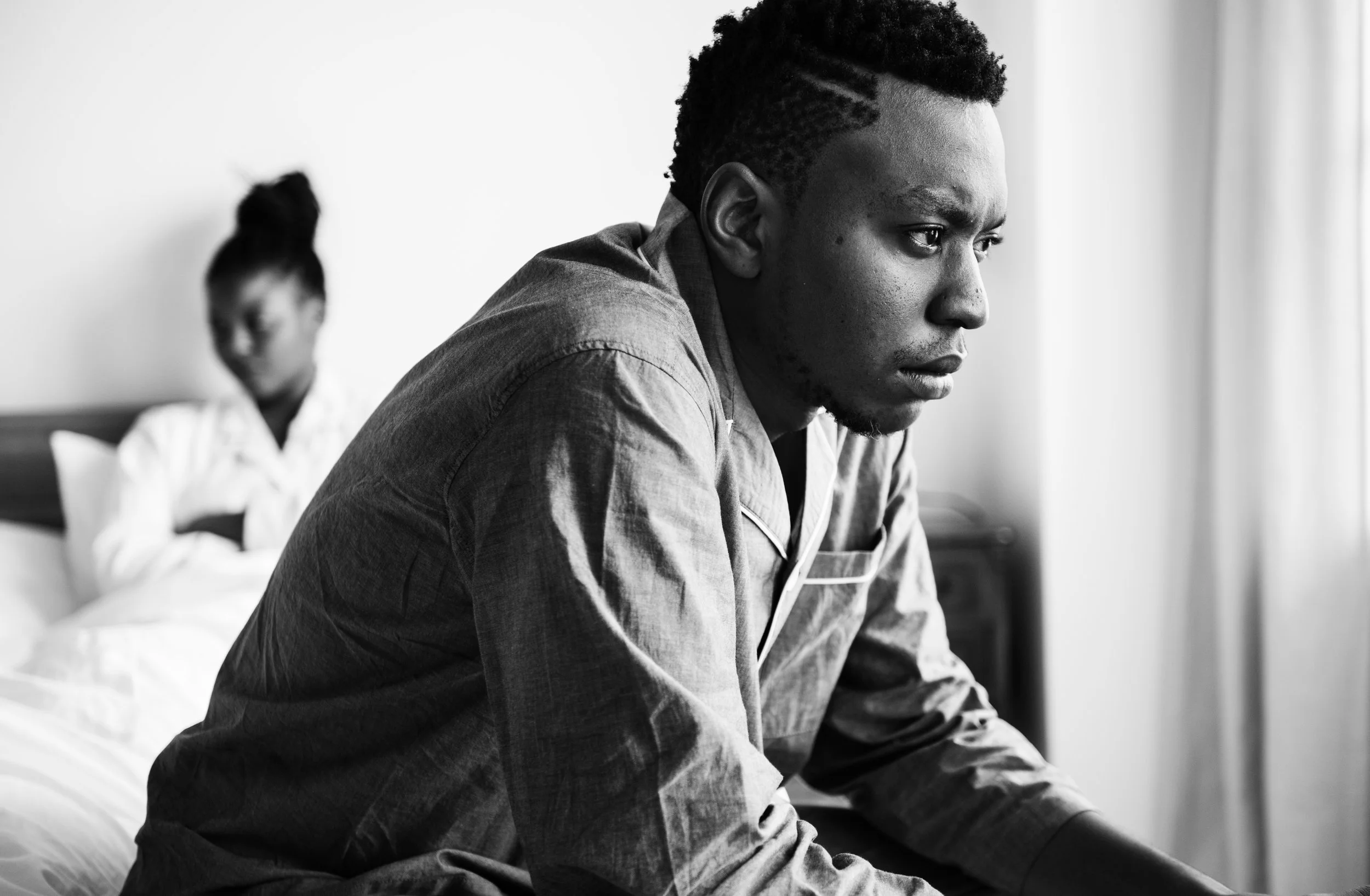 Black couple sitting apart in bedroom, man looking away, postpartum relationship disconnection