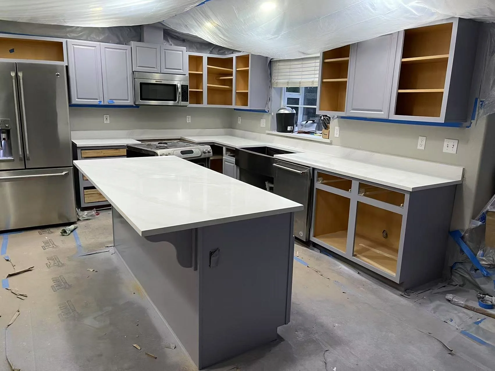 Kitchen under renovation with space for cabinets, appliances, and a kitchen island, partially finished with some open shelving, a microwave, and a refrigerator.