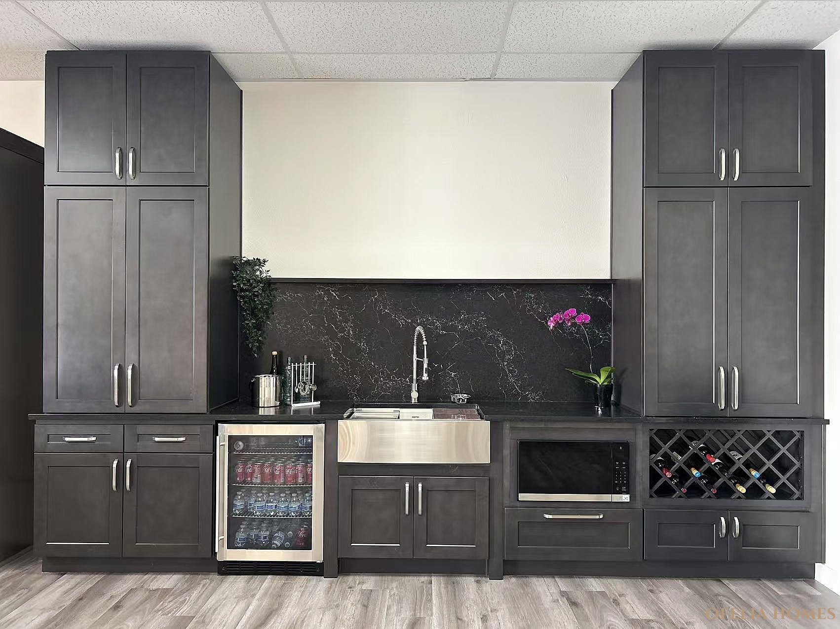 Modern kitchen with dark cabinets, stainless steel appliances, wine rack, and a small refrigerator. Features a black marble backsplash, gray flooring, and decorative plants.