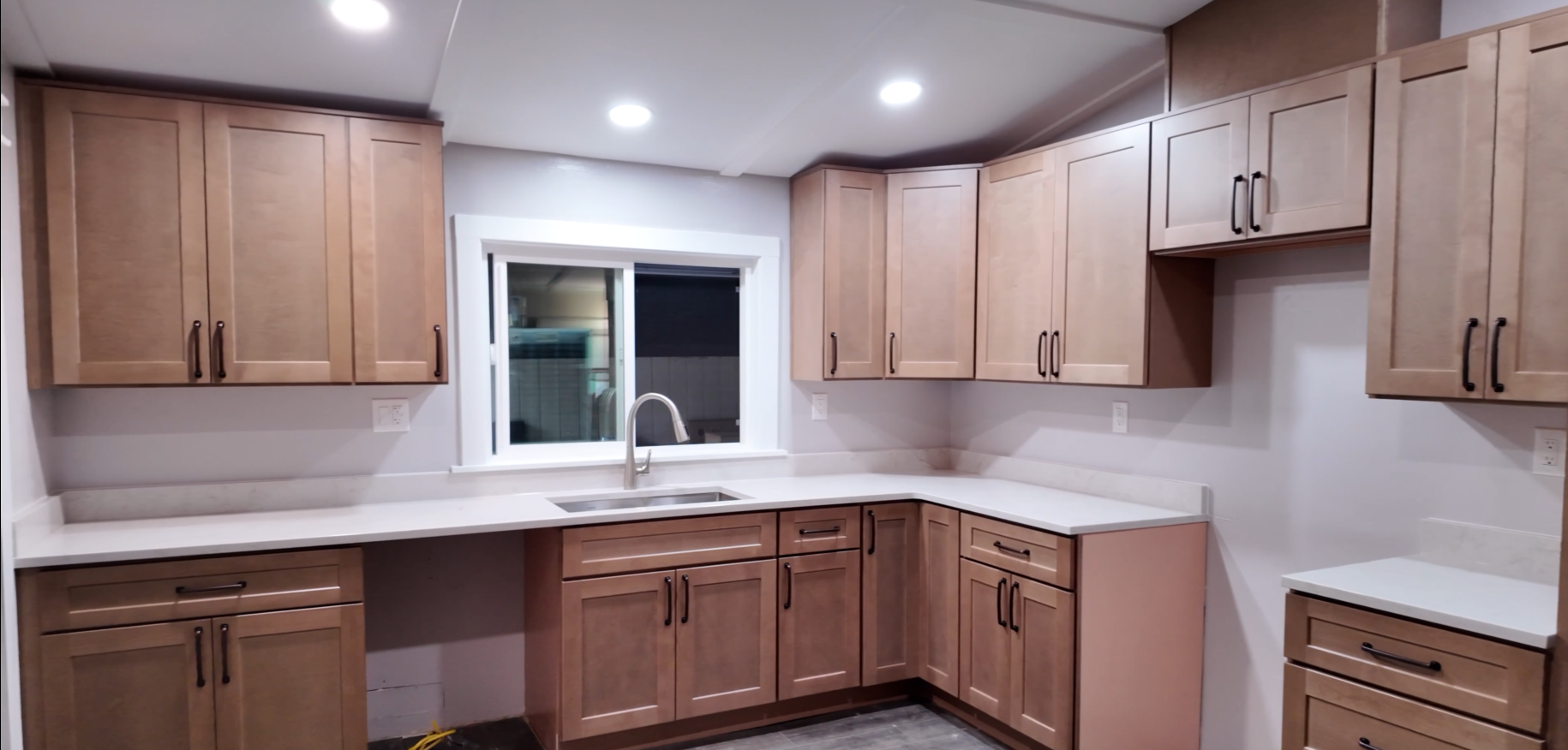 Kitchen with wooden cabinets, white countertops, a window above the sink, and a faucet. Recessed lighting on the ceiling.