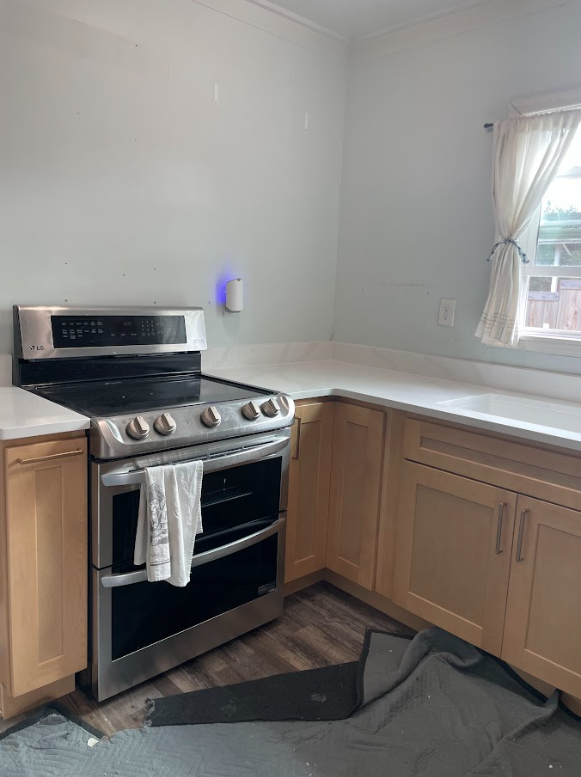 Kitchen with beige cabinets, a stainless steel stove, and a window with curtains.