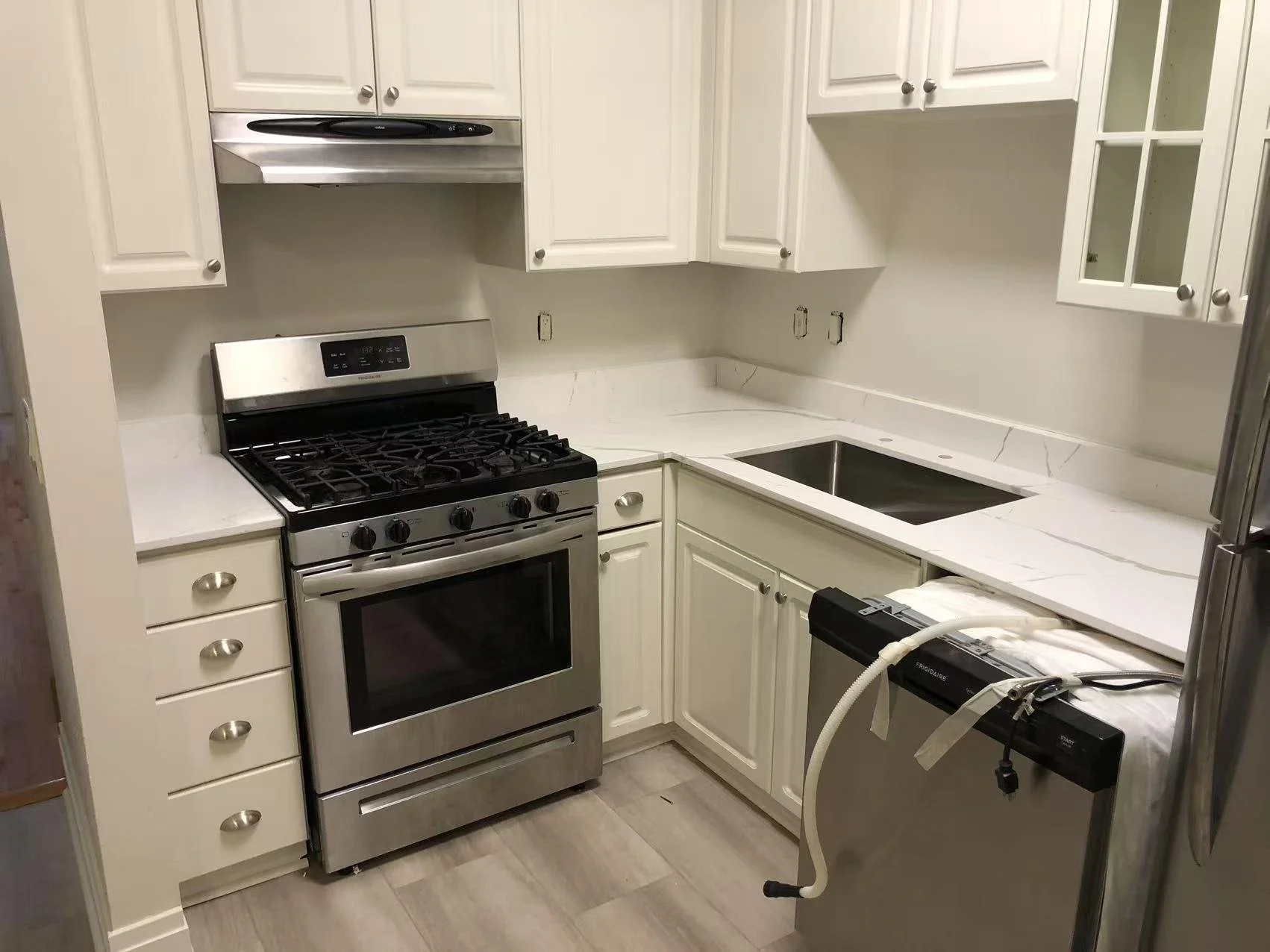 Kitchen in progress of renovation with white cabinets, marble countertops, stainless steel stove, and a new dishwasher with installation braces.
