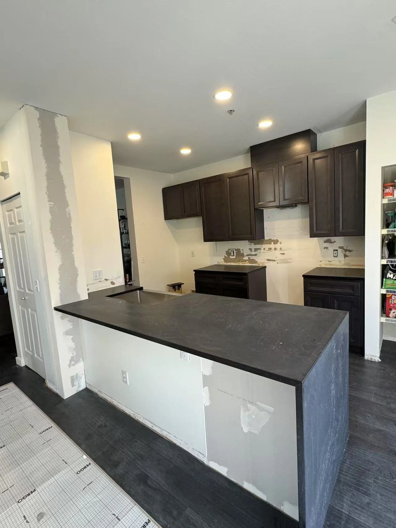 Kitchen under renovation, dark cabinets installed, partially painted walls, unfinished backsplash, and a large dark countertop on an island.