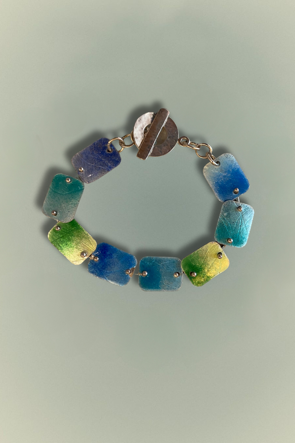 Handcrafted Tidal Hues Bracelet featuring vibrant blue and green vitreous enamel links set on fine silver, finished with a sterling silver toggle clasp. Designed by Linda Lewis.