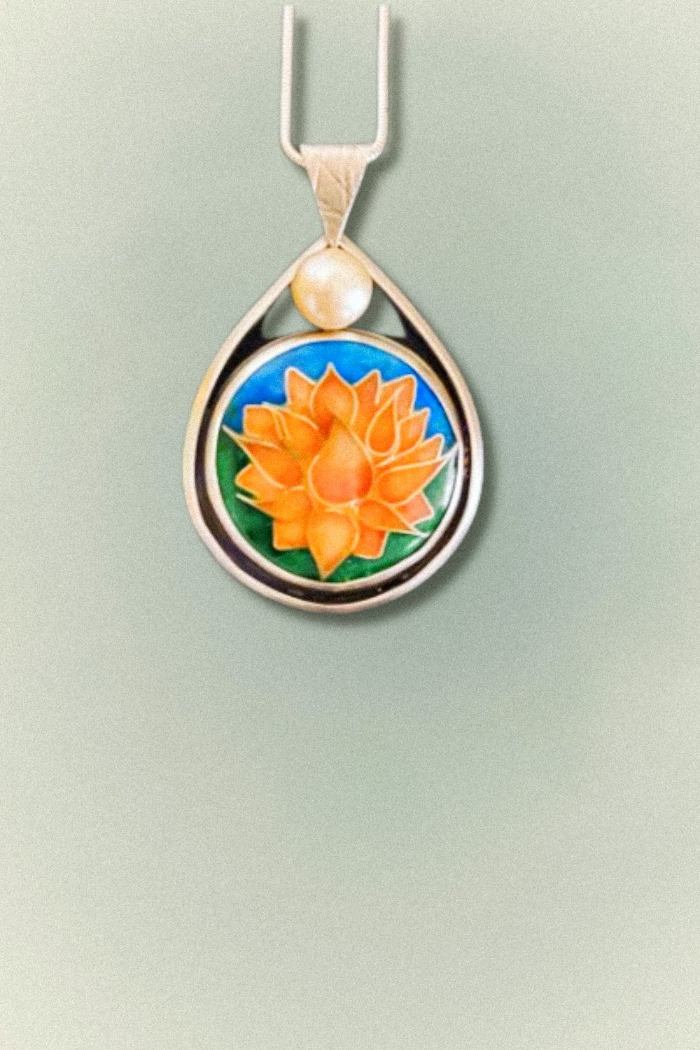 A handcrafted enamel pendant featuring an orange lotus flower with a pearl accent, set in sterling silver.