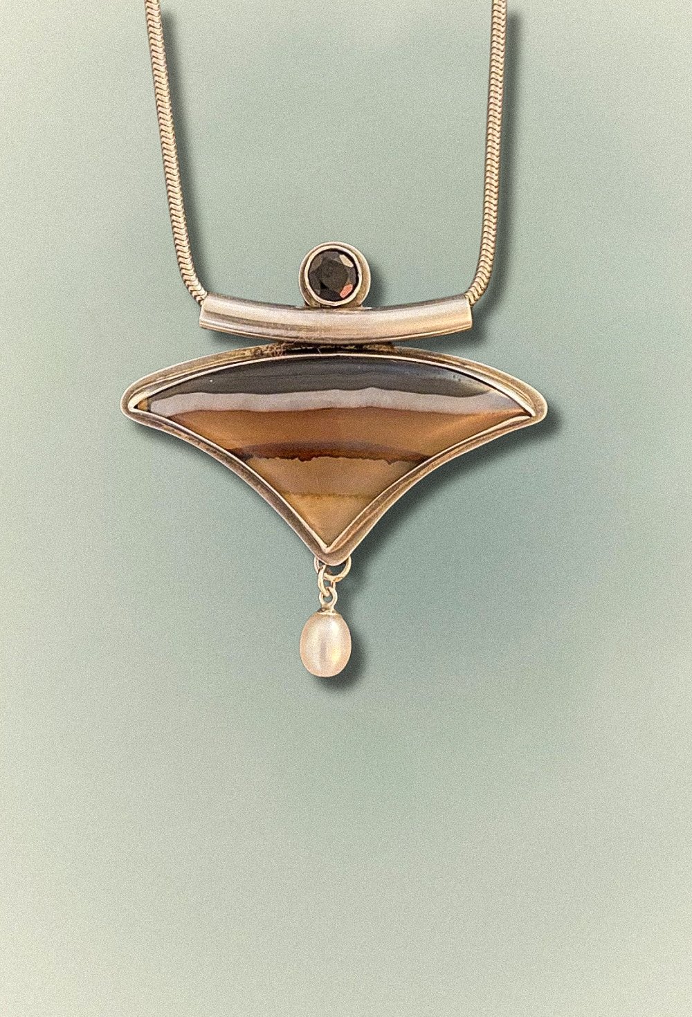 A handcrafted pendant featuring layered agate, polished onyx, and a freshwater pearl set in sterling silver.