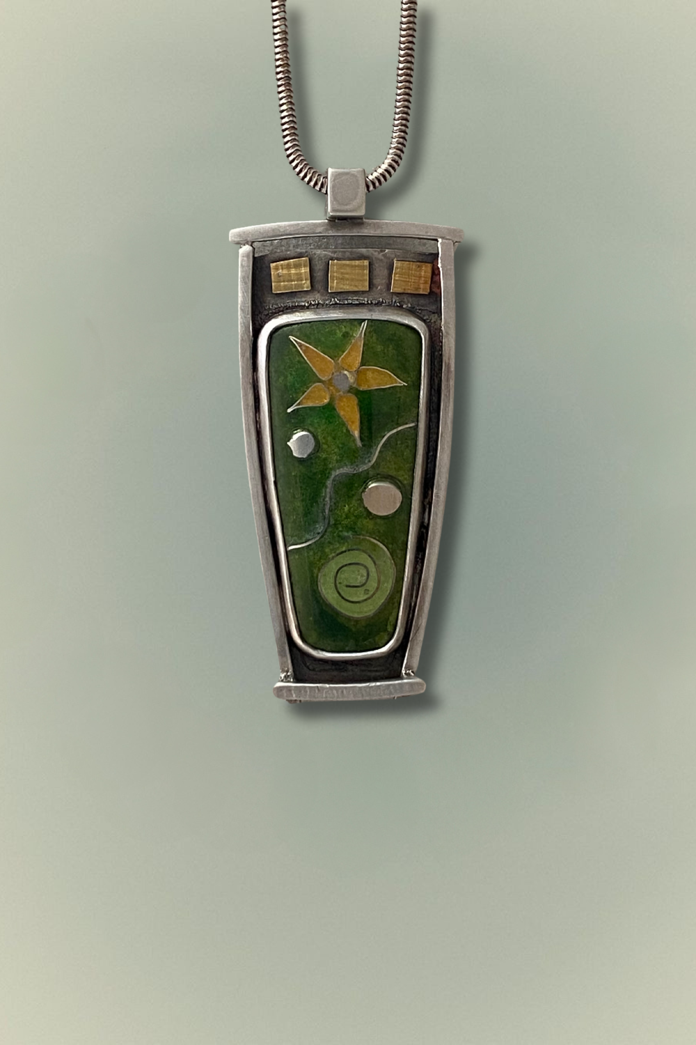 A handcrafted cloisonné pendant featuring a sunflower design on a green background, framed in sterling silver.