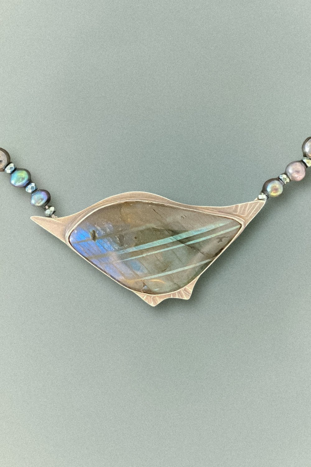 A sterling silver bird pendant with a labradorite stone, accented by pearls and hematite beads, on an 18-inch necklace.