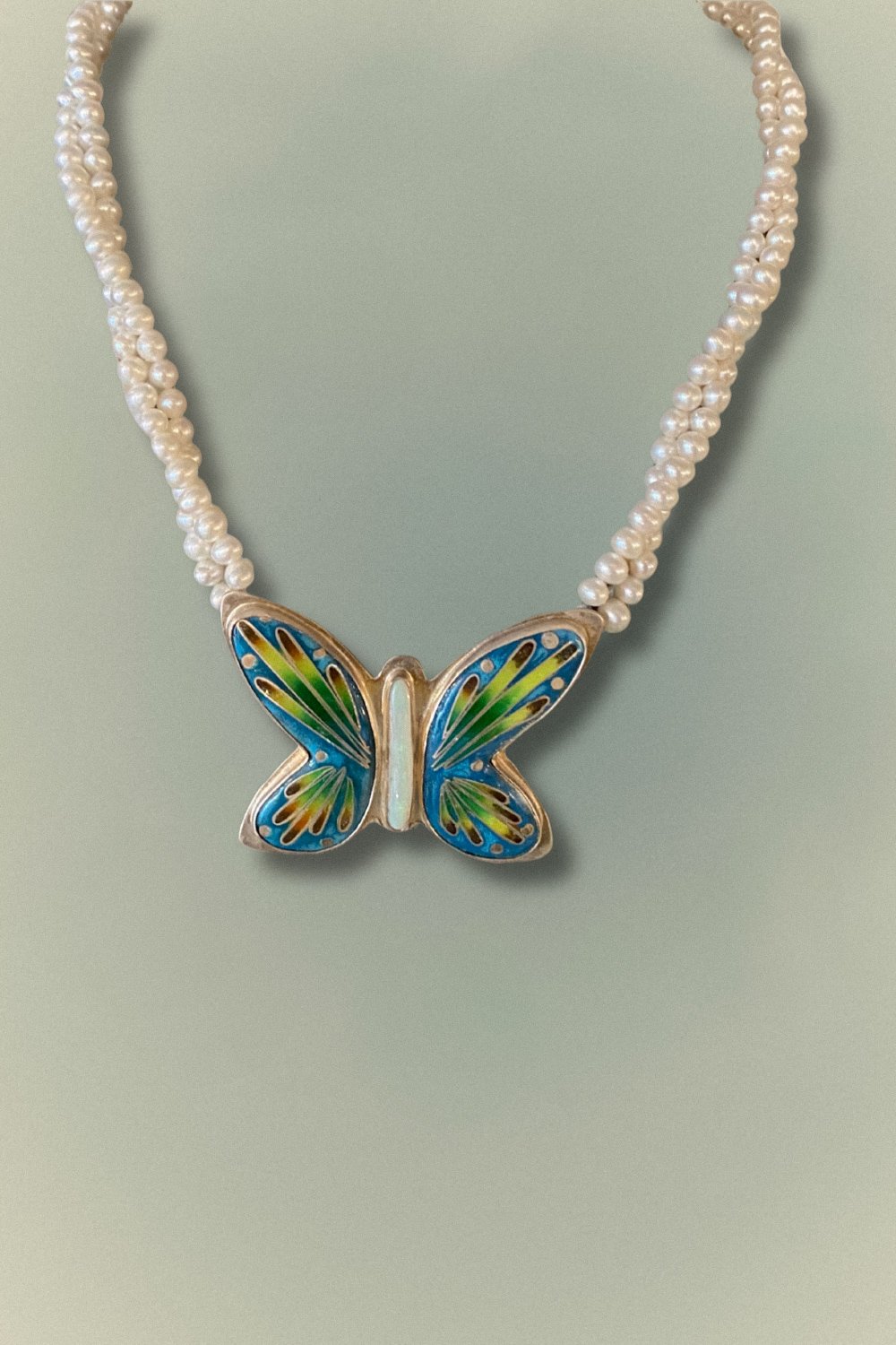 A handcrafted butterfly pendant necklace featuring cloisonné enamel and a strand of freshwater pearls.