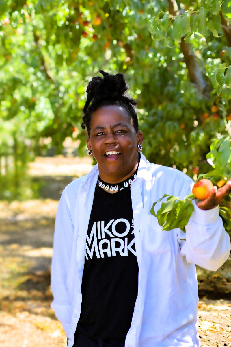 C. Njoube Dugas, Co-Founder of Saba Community Food Alliance, stands in a peach field on a Bay Area farm.