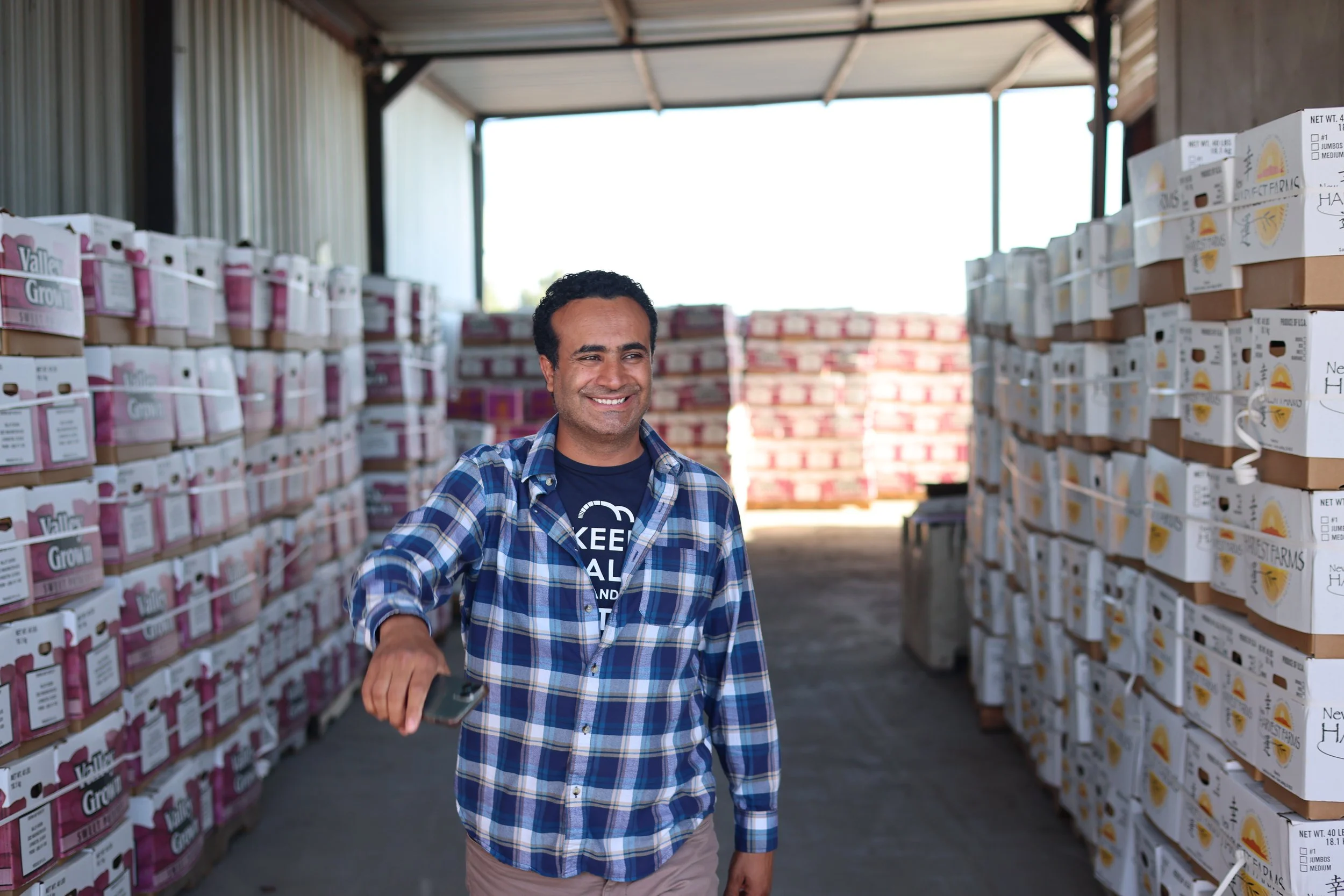 Dave, a BIPOC farmer in a California warehouse, smiling as he oversees the ethical sourcing and distribution of fresh produce for Saba Community Food Alliance, enhancing food service quality and community health