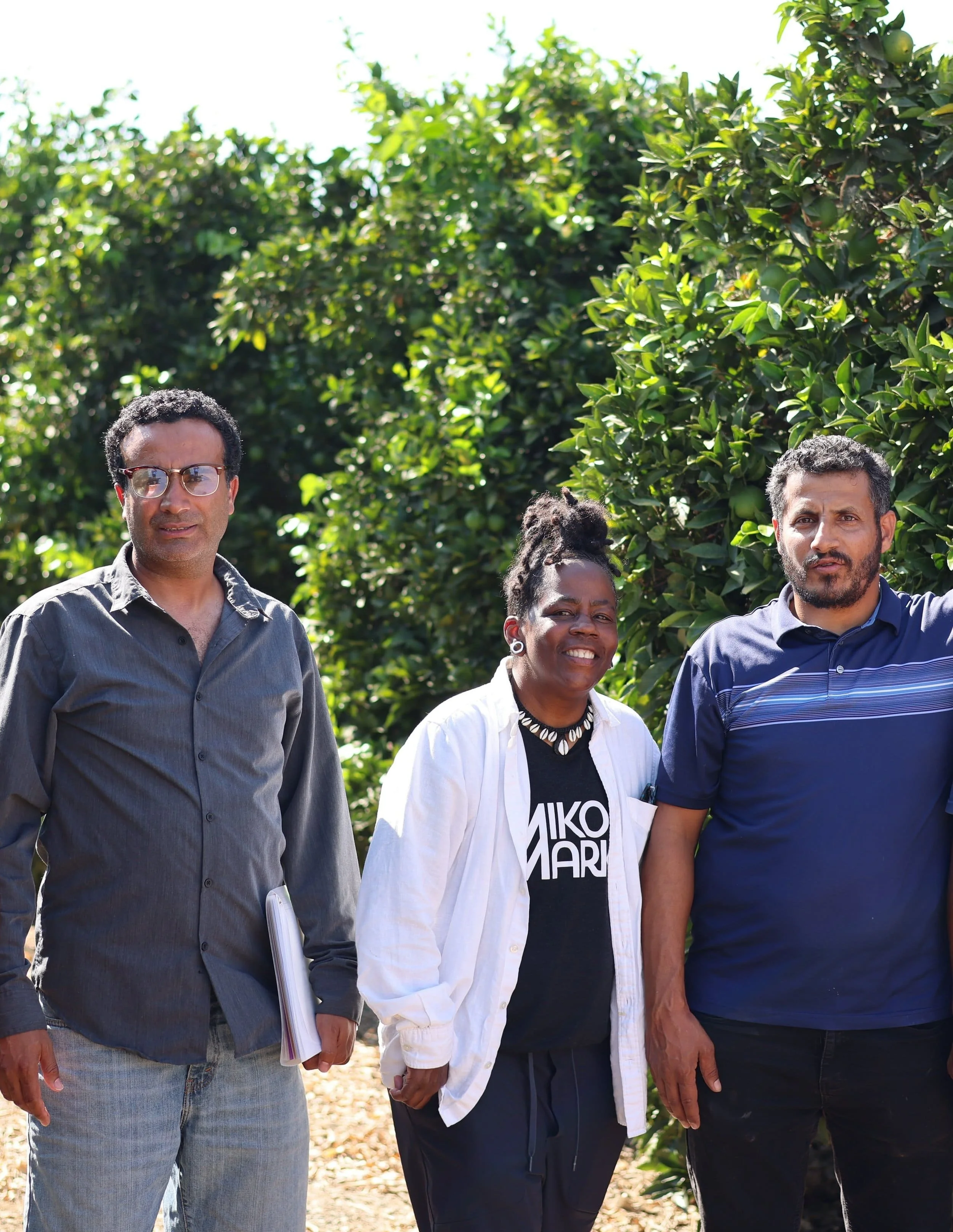 The founders standing together in front of lush green trees, possibly in an orchard, representing the collaboration between Saba Community Food Alliance and local BIPOC farmers to support ethical food sourcing and distribution in the Bay Area