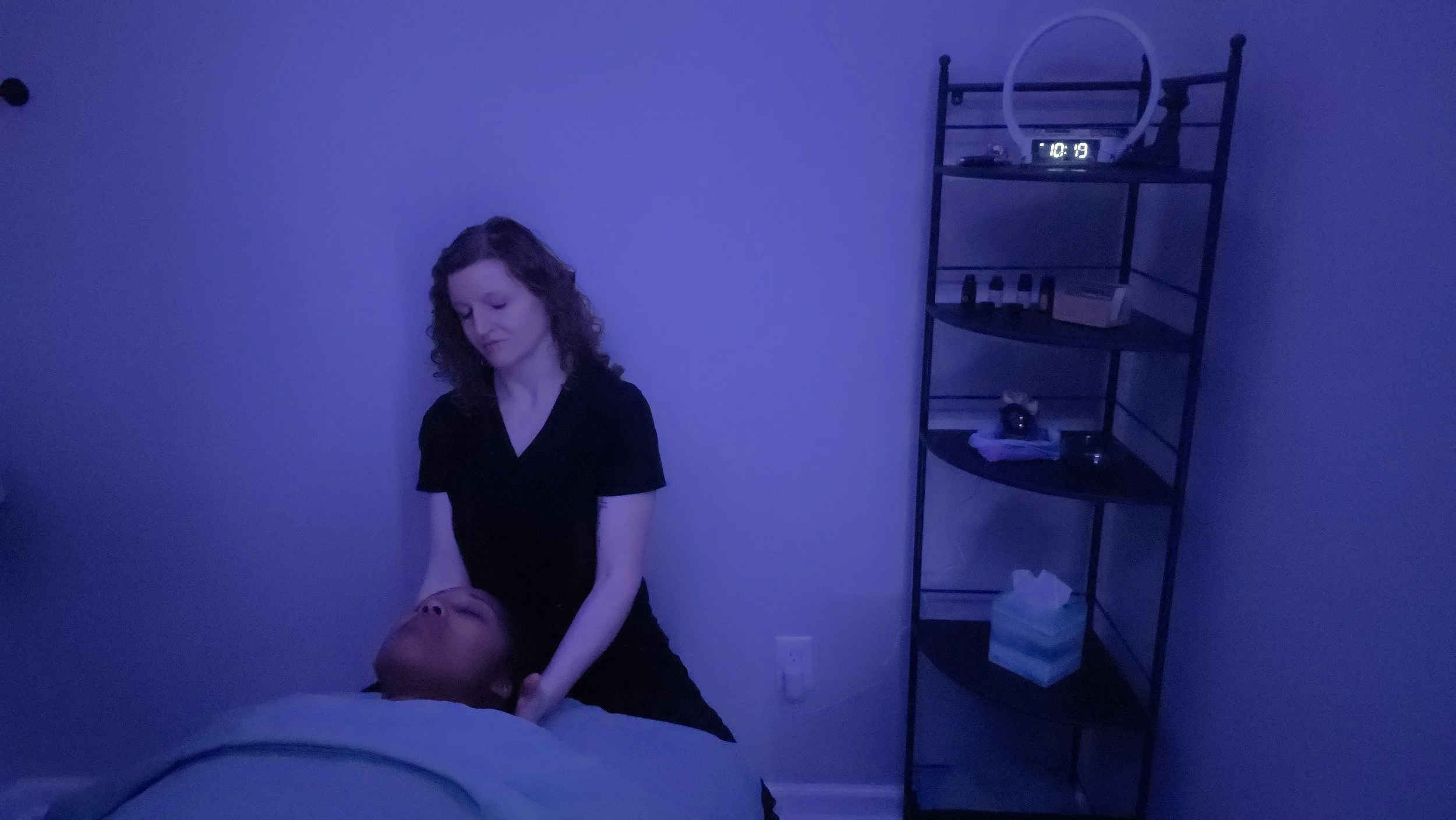 Picture of Ashley Mack, Licensed Massage Therapist providing neck and shoulder massage in massage room with essential oils in the background.