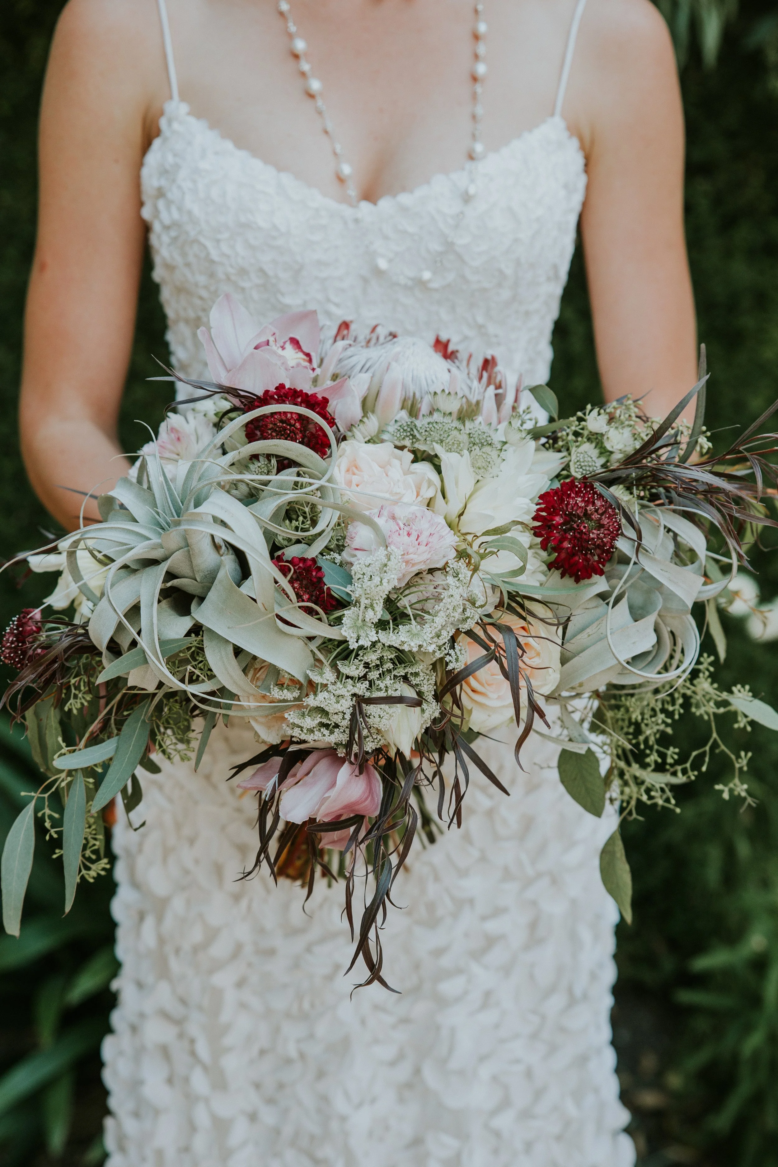 bride holding bohemian and earthy bouquet with sage, maroon, light pink color palette designed by denver wedding planner