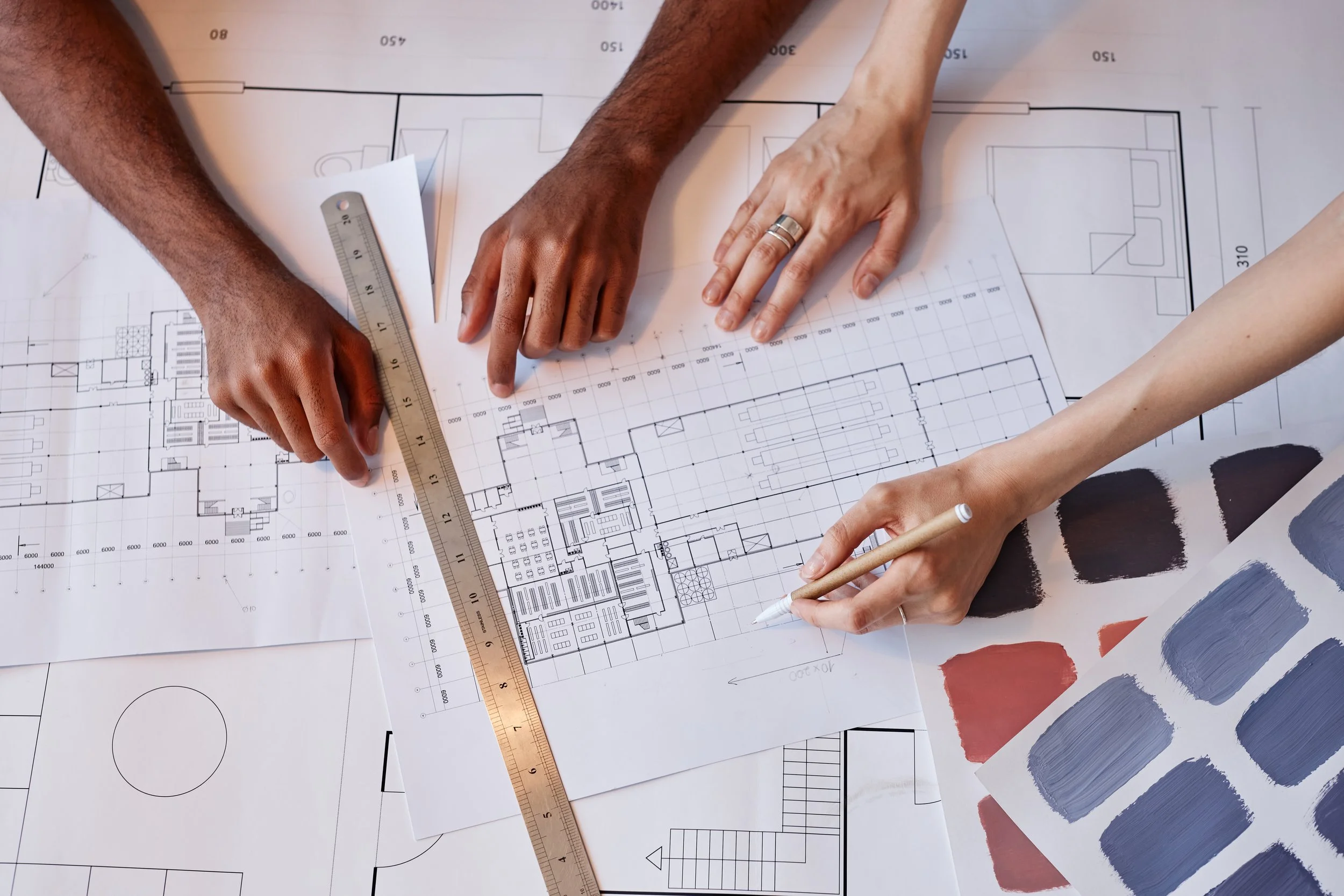 Two people working on architectural blueprints, with one using a ruler and the other drawing with a pencil.