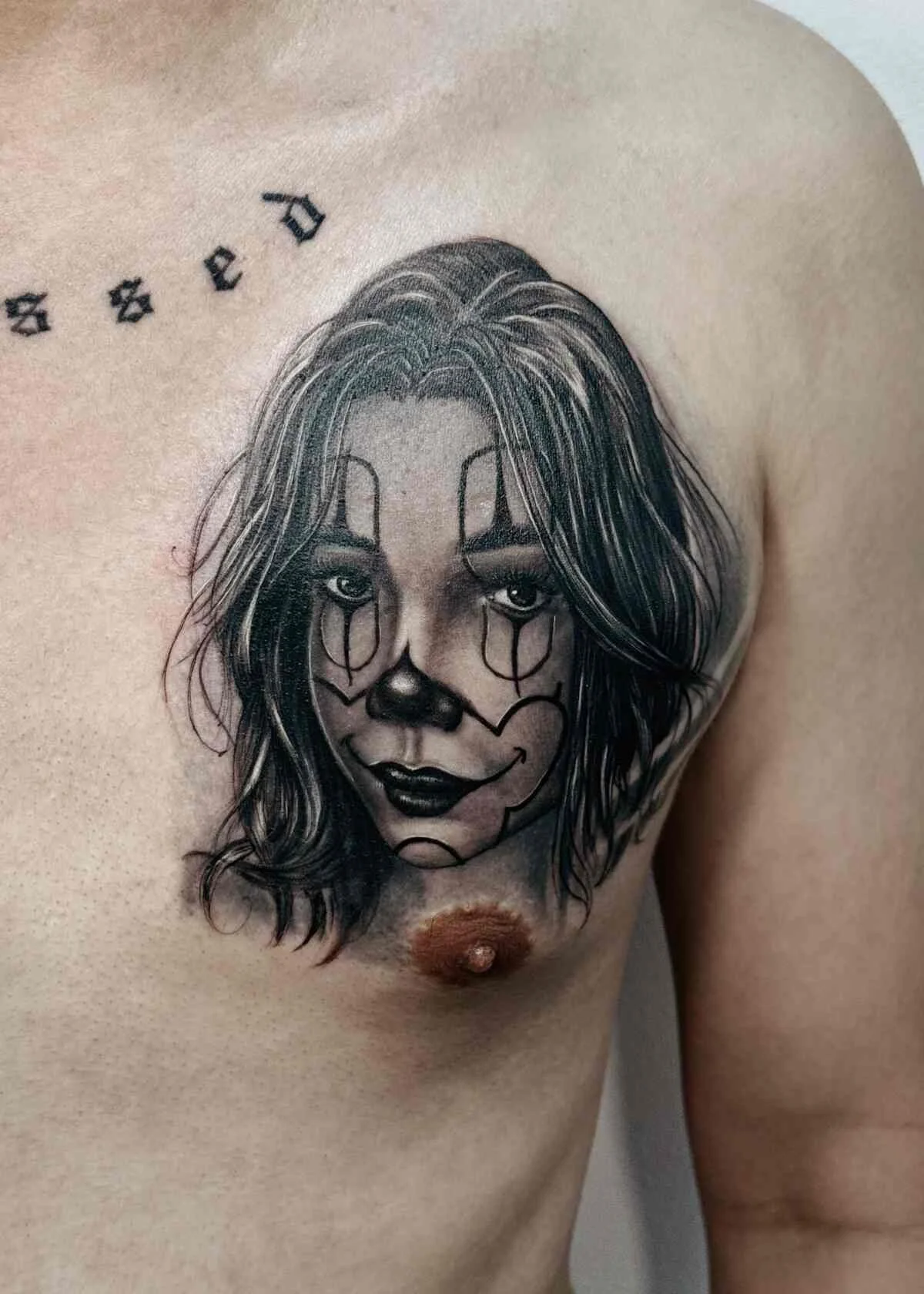 Tattoo of a woman's face with makeup and long, wavy hair, blending into a clown skull face design on the person's chest.