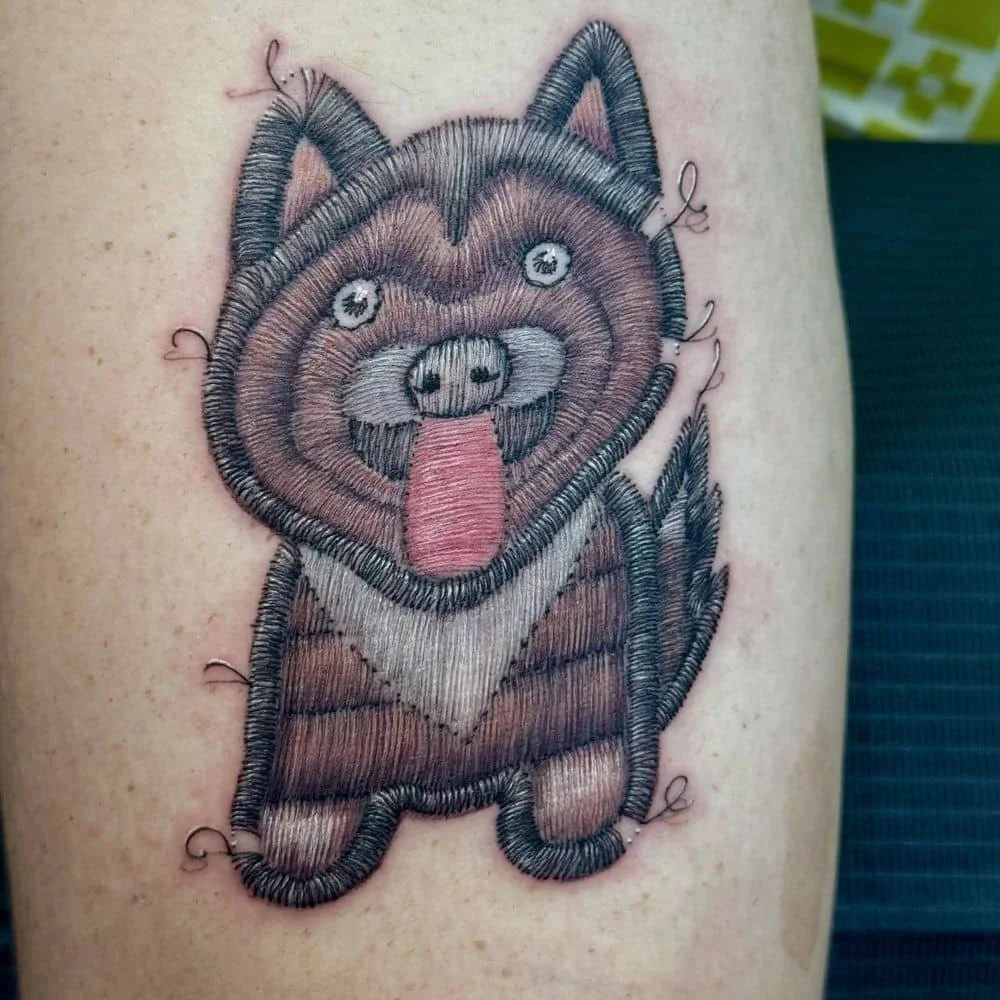 Embroidery tattoo of a happy dog with its tongue sticking out, stitched with various colored threads.