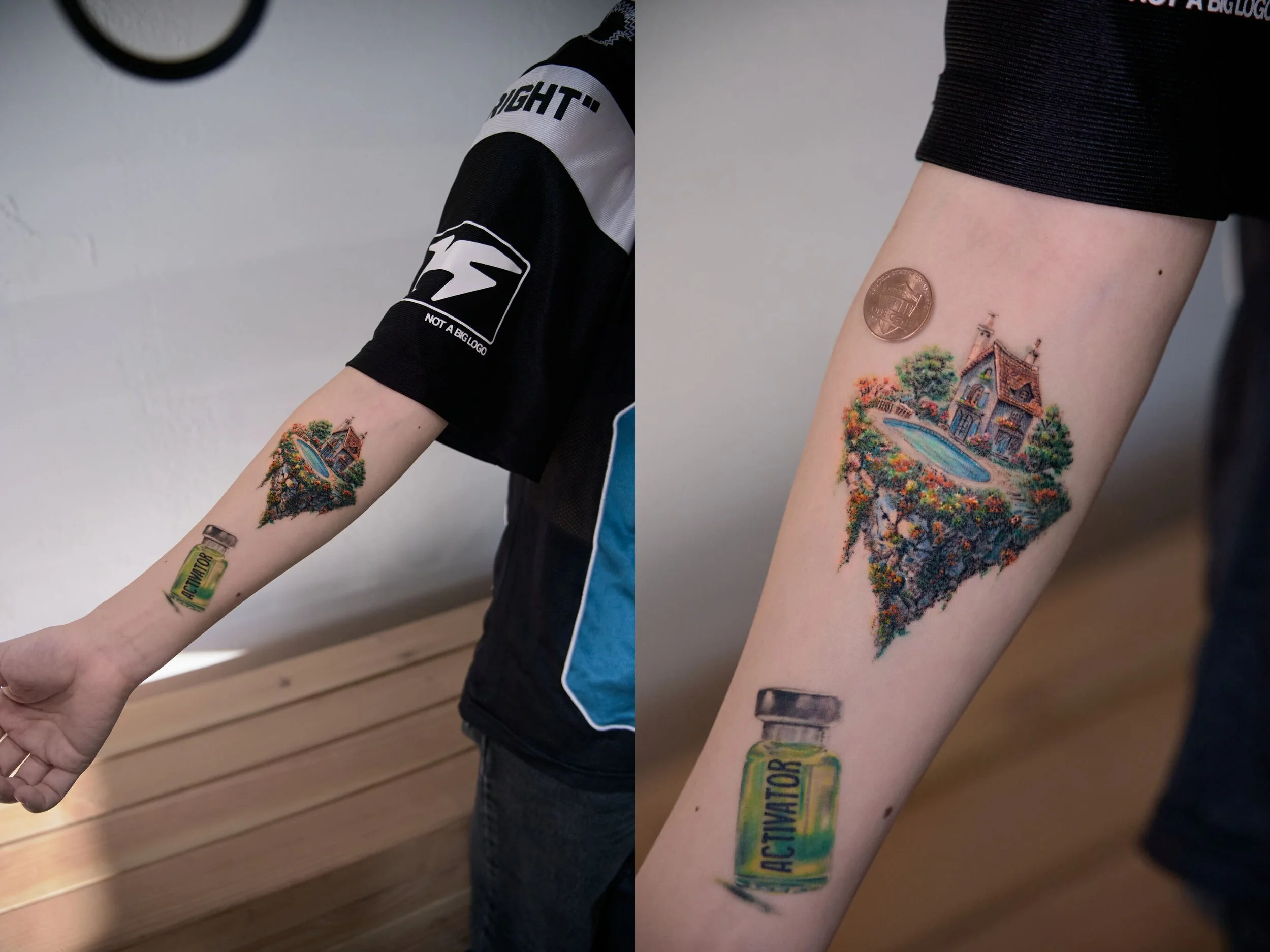 Tattoo of a colorful house with a pond, surrounded by trees, on a person's inner forearm, with a penny and a vitamin bottle labeled 'Activator' nearby.