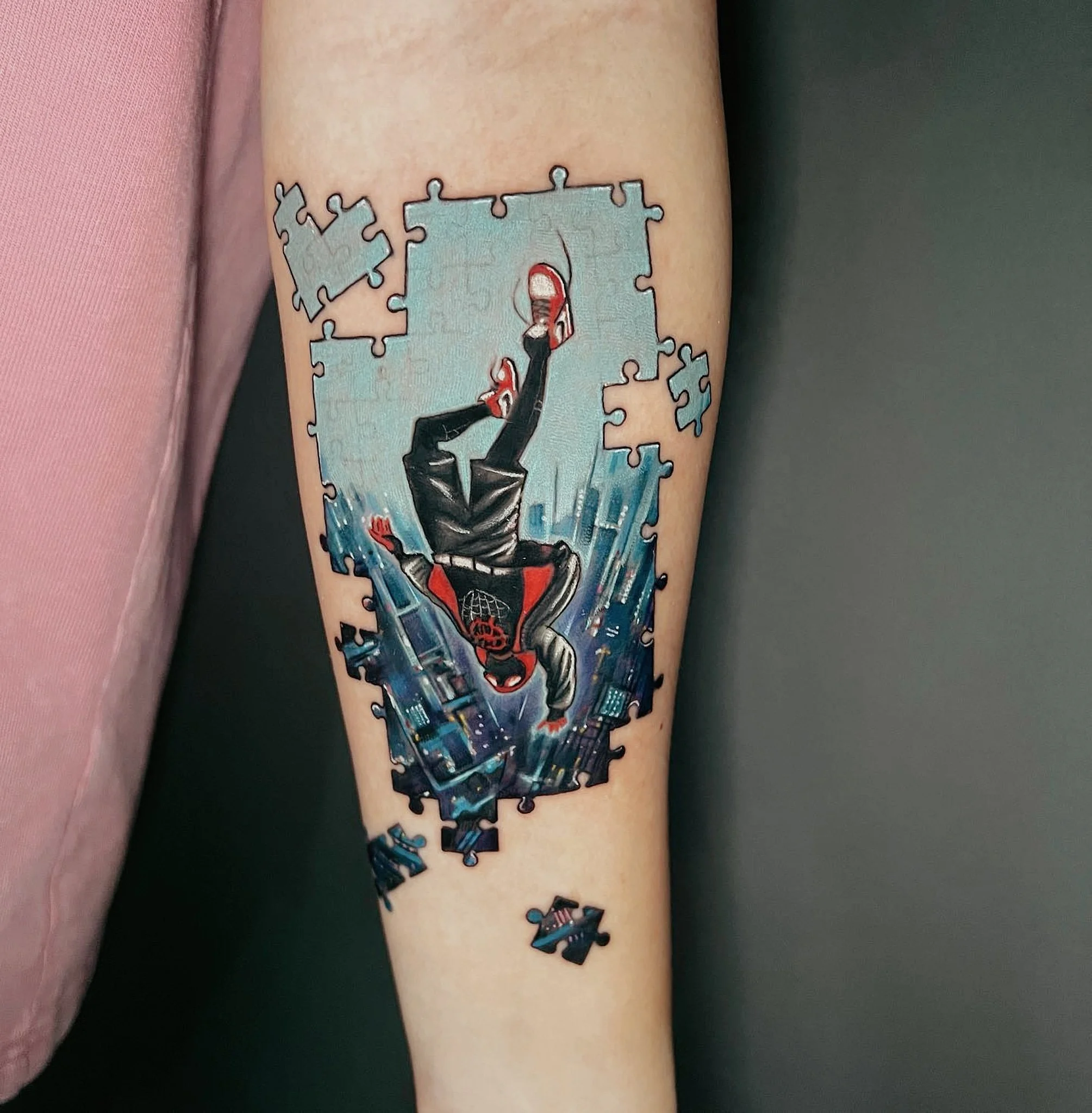 Tattoo of Spiderman with a web-shooting pose, made with colorful puzzle pieces on a person's arm.
