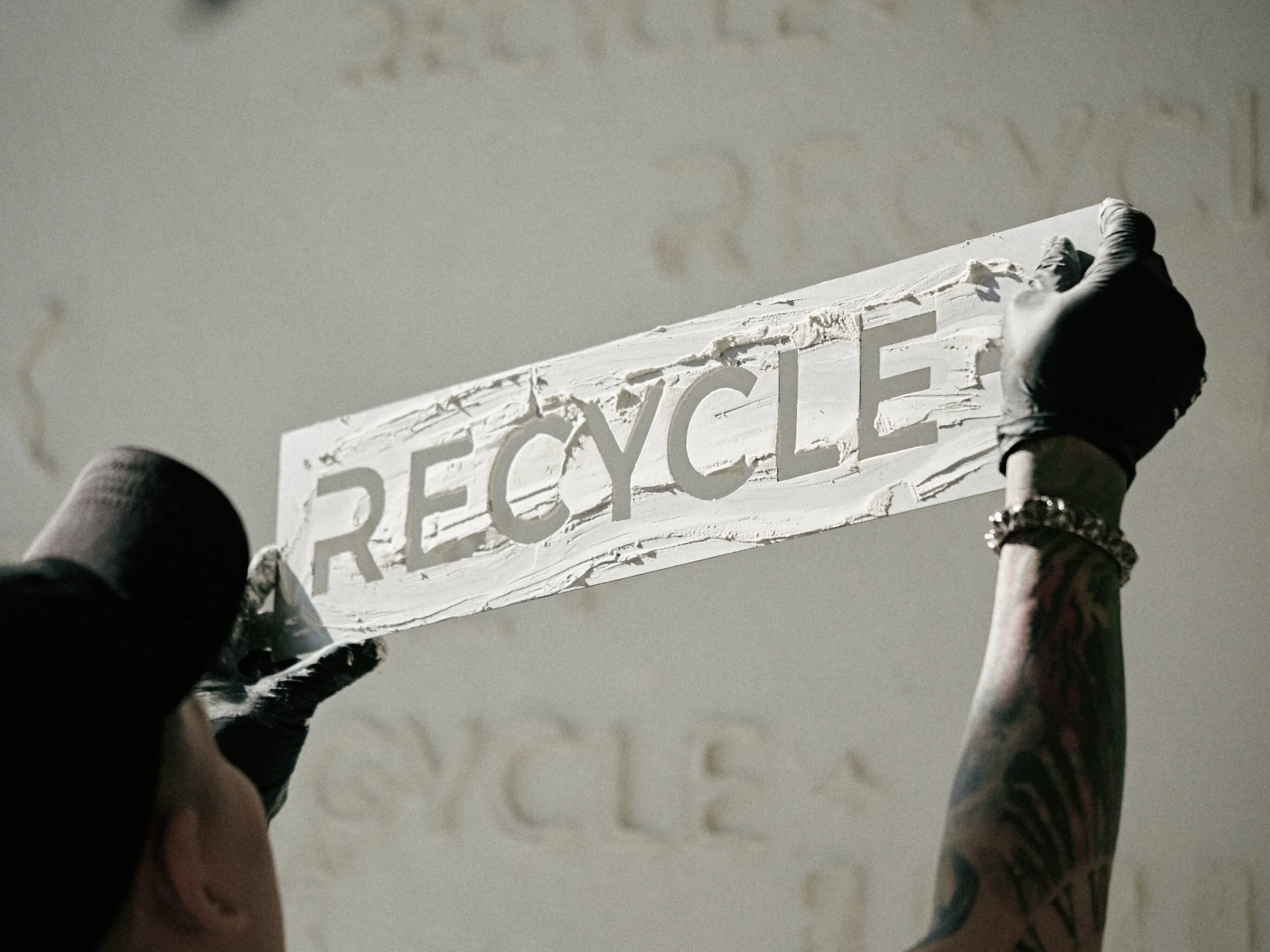 A person with tattoos on their arm holding a wooden sign with the word 'RECYCLE' cut out.