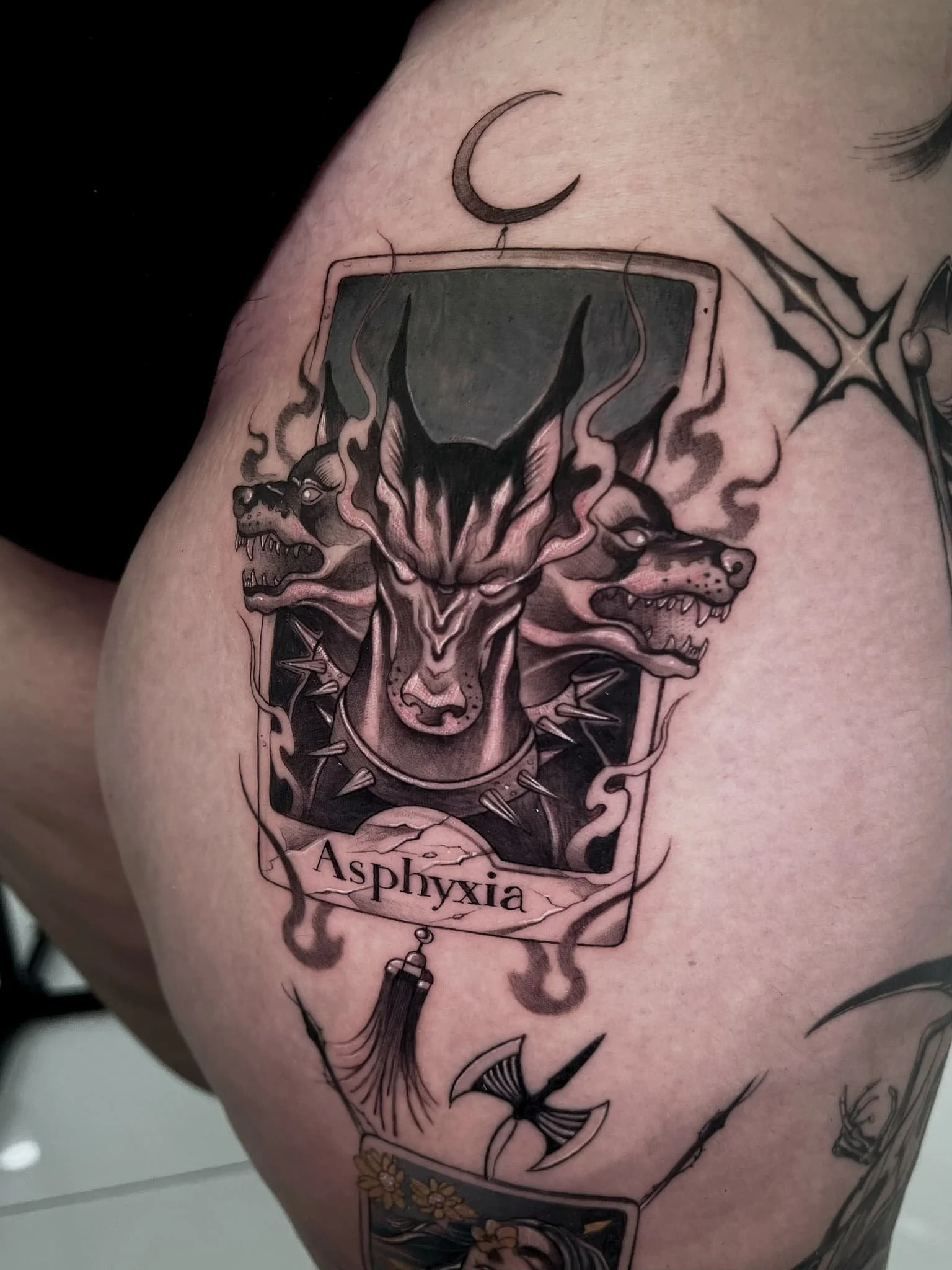 Black and white tattoo featuring a central snarling wolf with flames, a pair of snarling lions, a crescent moon above, and the word 'Aphyxía' below, all surrounded by decorative elements.