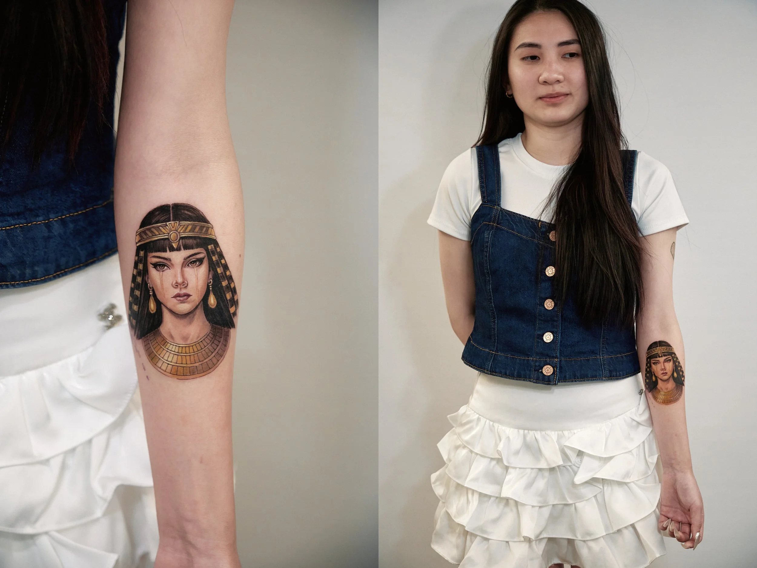 Young woman with long black hair, wearing a white t-shirt, a denim vest, and a white ruffled skirt, showing a tattoo of an Egyptian queen on her forearm