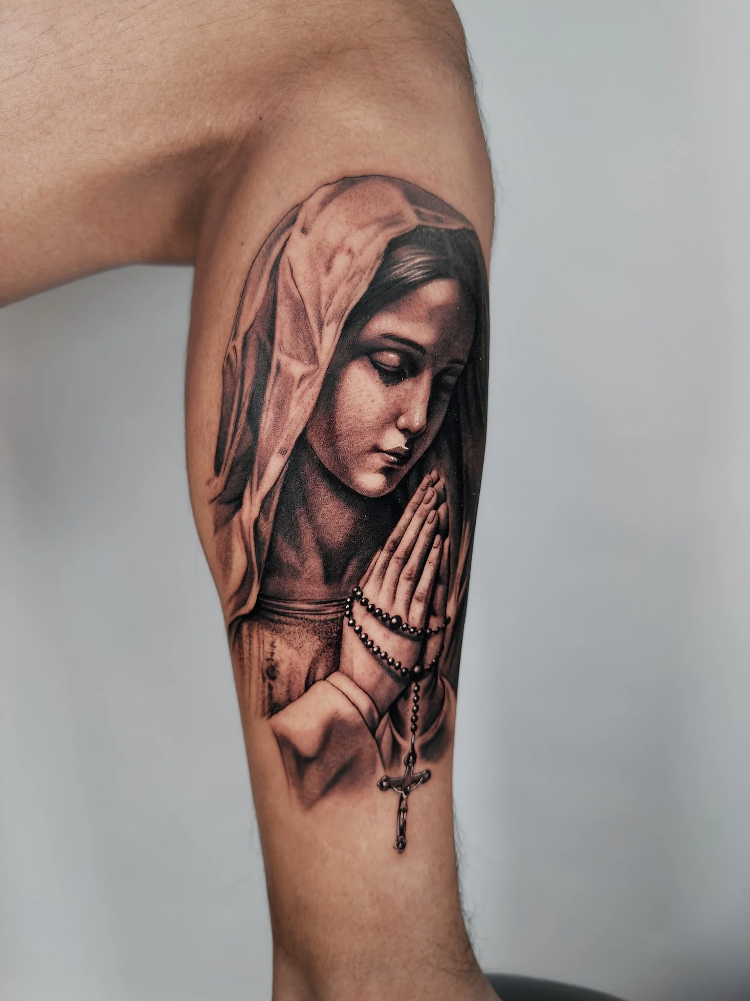 Tattoo of a praying woman with a rosary on forearm