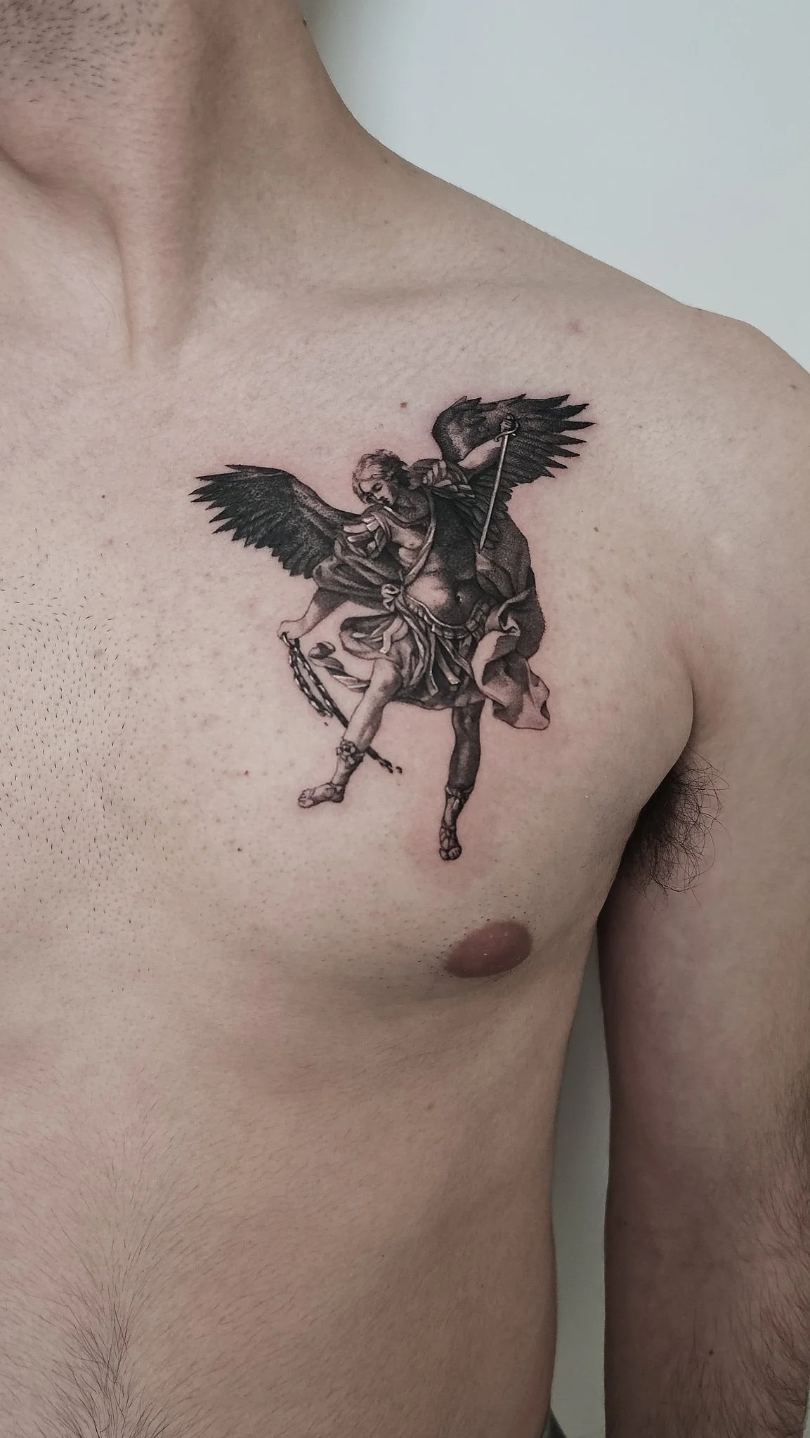 A detailed angel tattoo on a person's chest, featuring wings and armor.