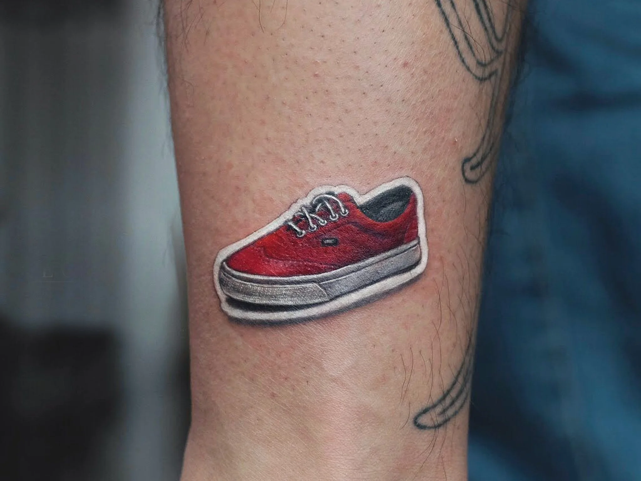 Custom color tattoo on the arm by Binx at Recycle Tattoo, featuring a vibrant red sneaker with crisp white detailing. The piece highlights realistic textures and bold color saturation, showcasing clean linework and smooth shading to give the shoe a d