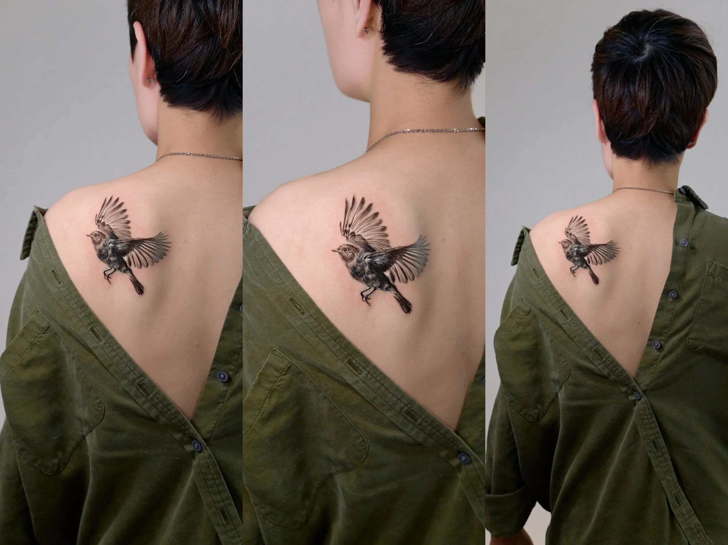 A woman shows a tattoo of a bird in flight on her shoulder, wearing an open green shirt and a silver necklace, with short dark hair.