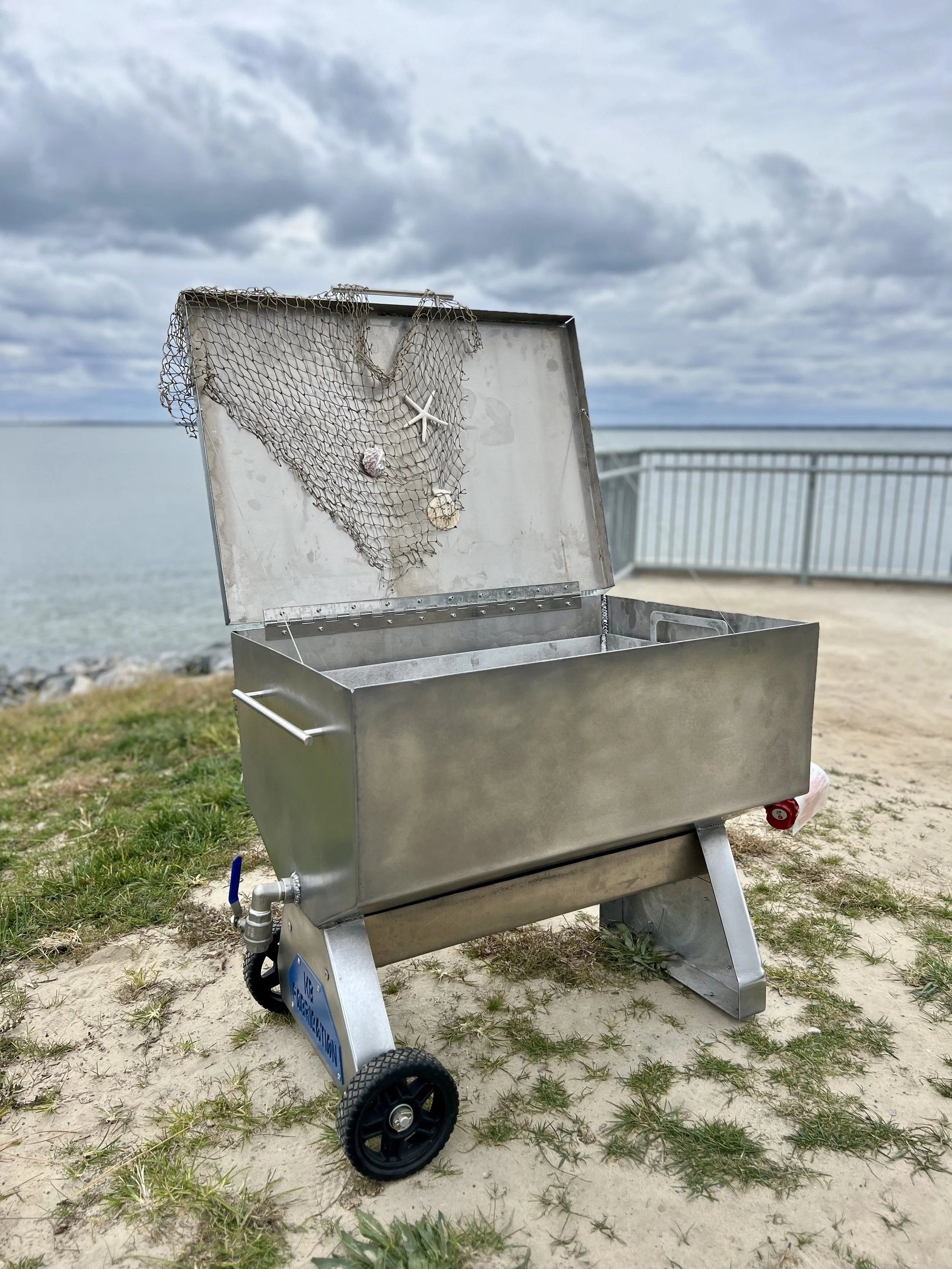 Open aluminum seafood steamer with decorative netting and shells by the water.