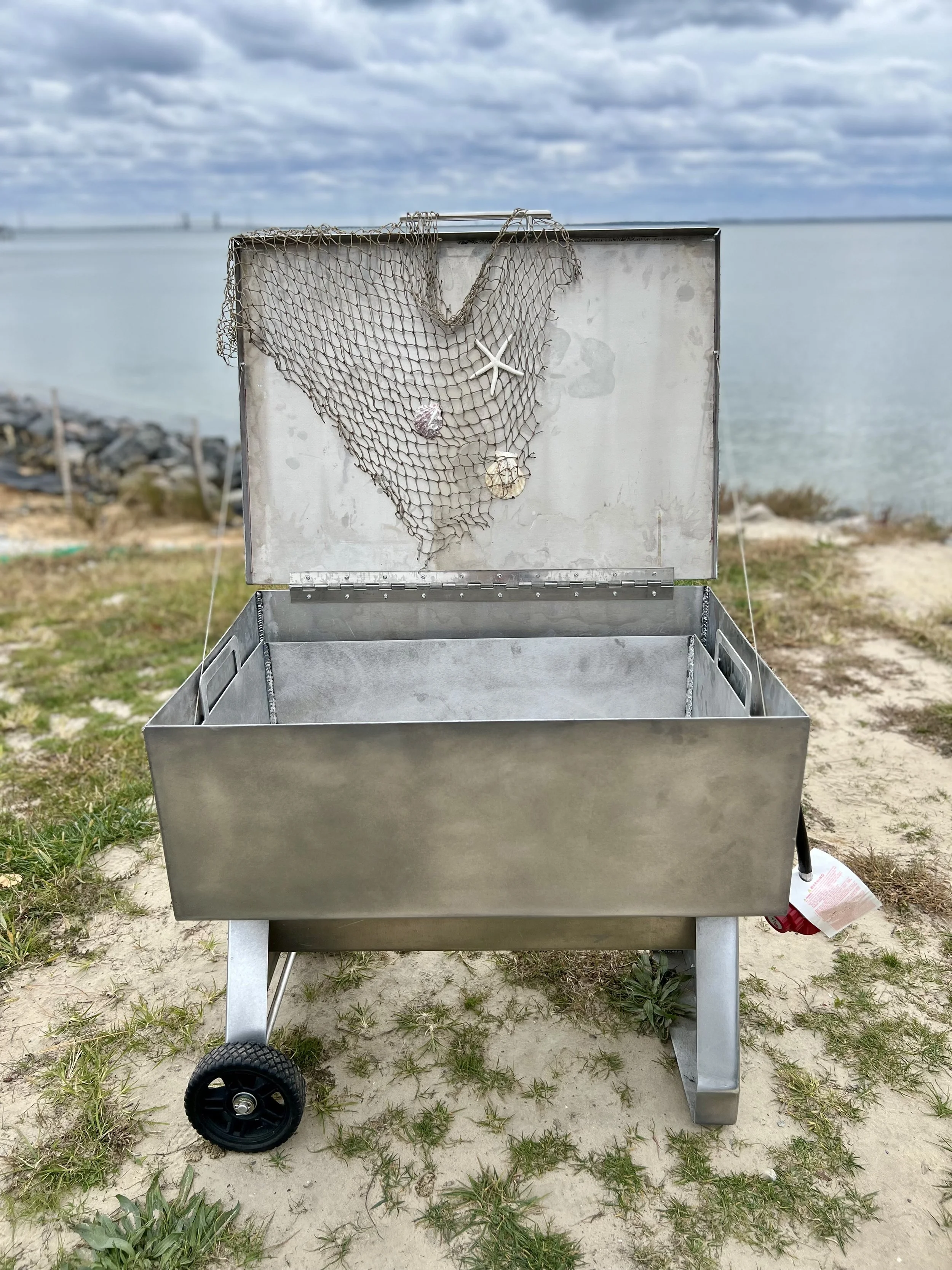 Open aluminum seafood steamer with decorative netting and shells by the water.