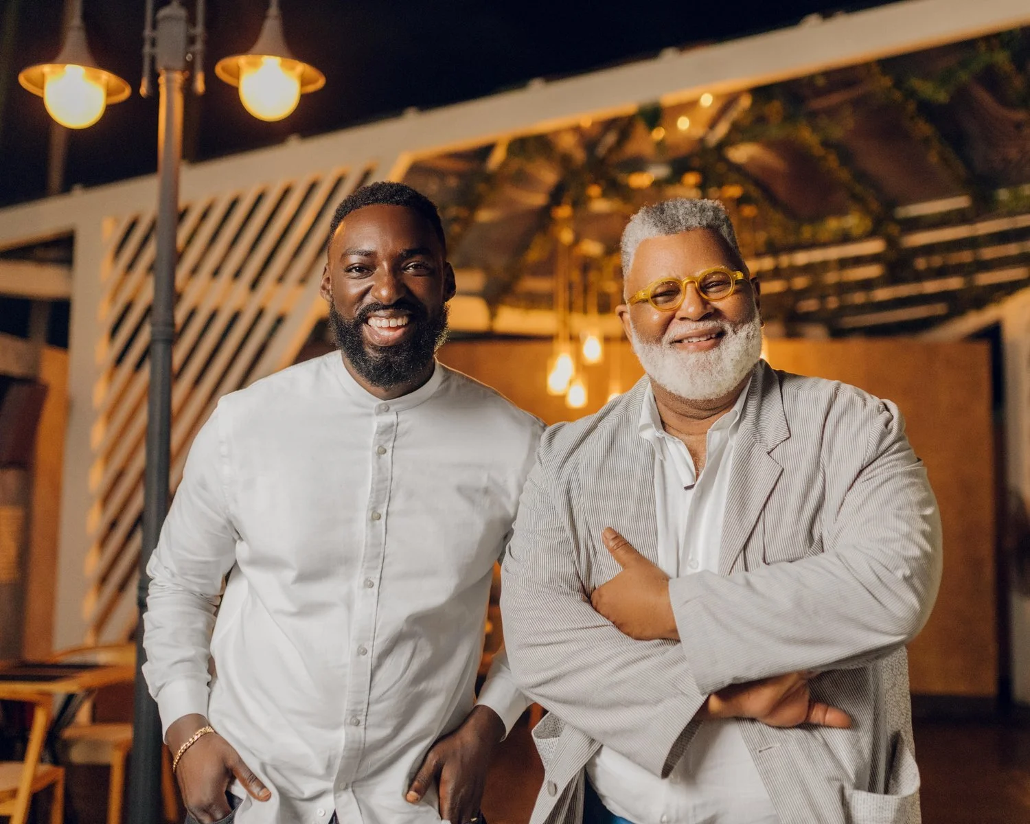 Chef Eric Adjepong and Alexander Smalls posing outdoors at night in a warmly lit setting.