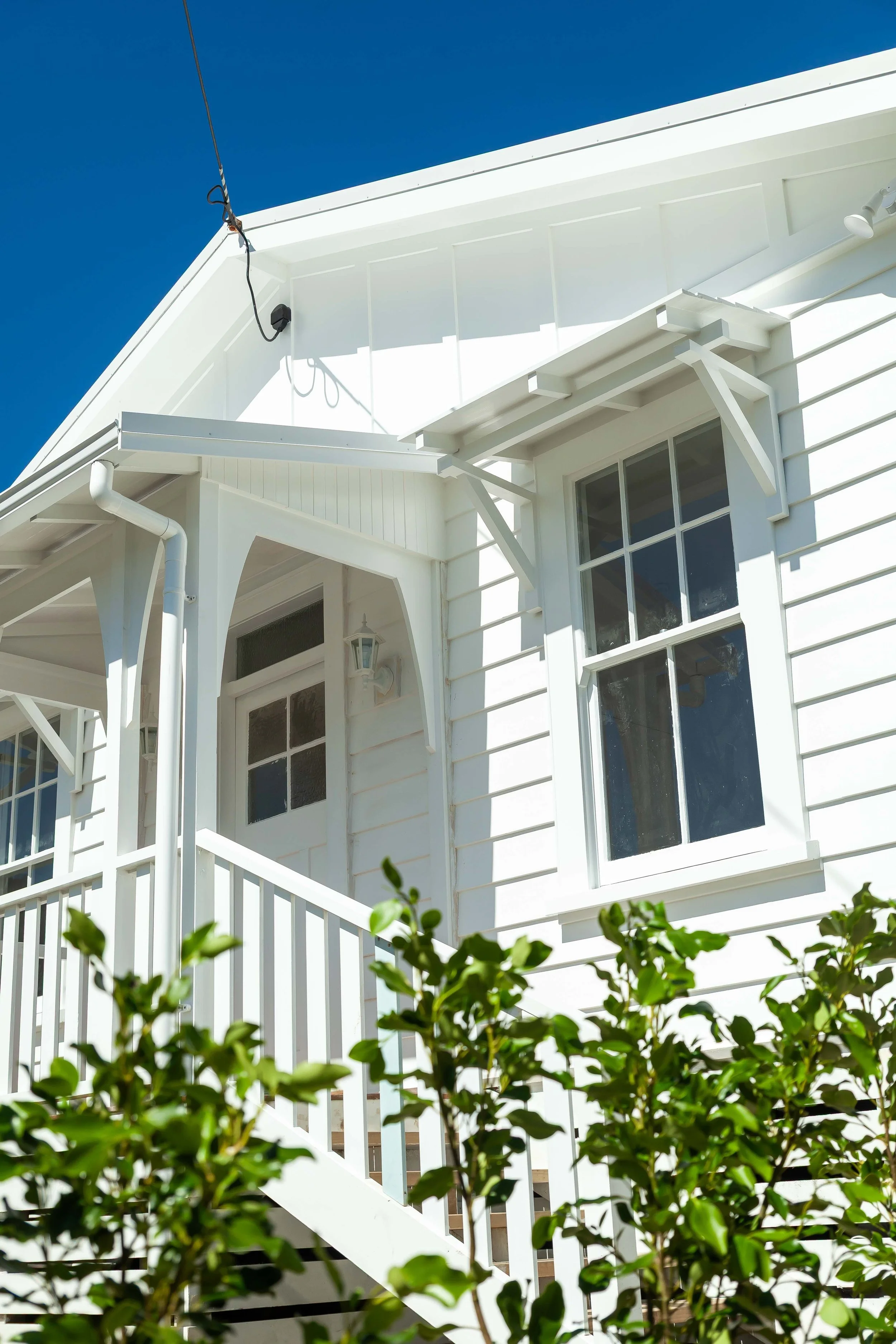Close-up of a white house with a porch, railing, and windows against a bright blue sky.