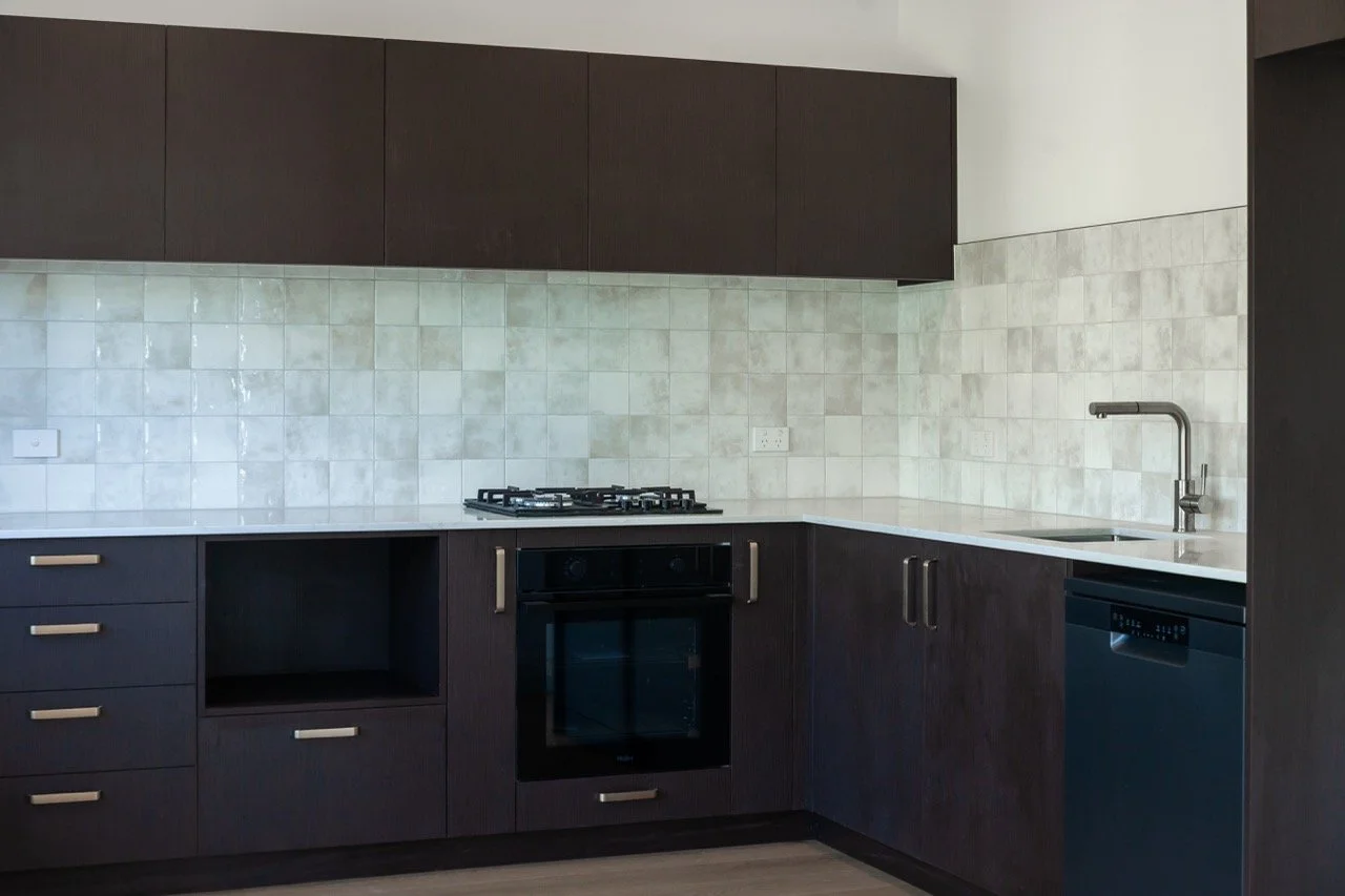 Modern kitchen with dark wood cabinets, a white countertop, a built-in oven, a gas stove, a sink with a chrome faucet, and a dishwasher, with a tiled backsplash.