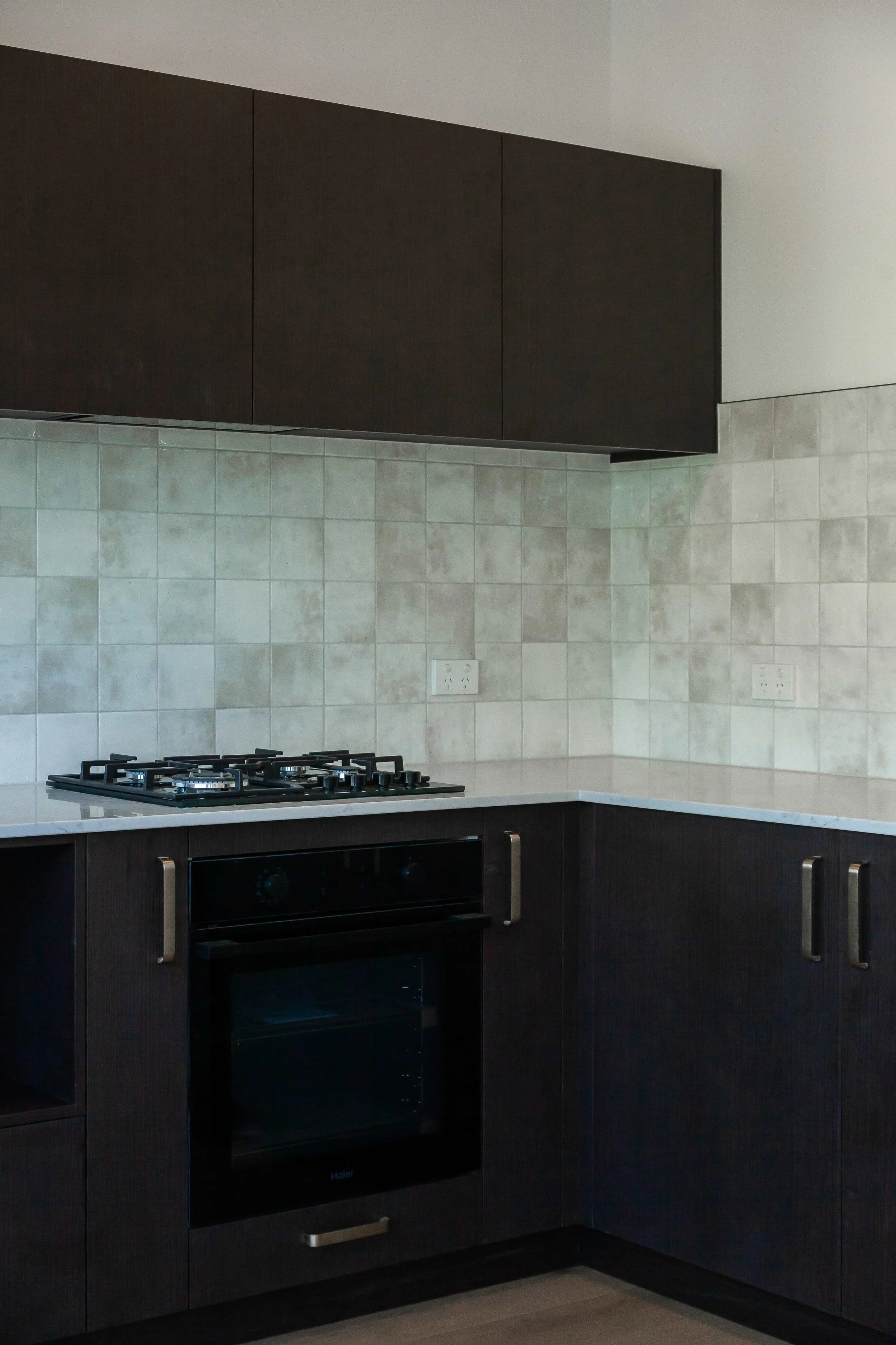 Kitchen with black cabinets, a gas stove and oven, a beige tiled backsplash, and two power outlets.