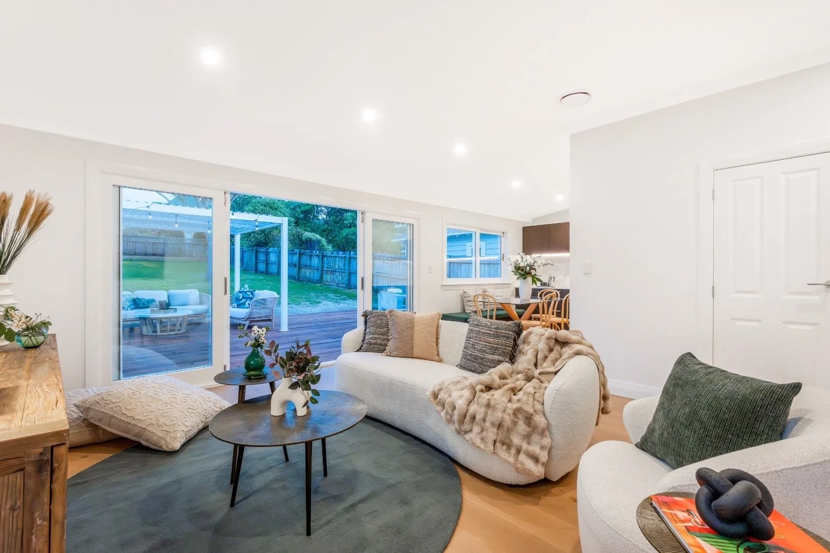 Bright living room with sliding glass doors opening to a backyard patio with outdoor furniture, white walls, and modern furnishings.